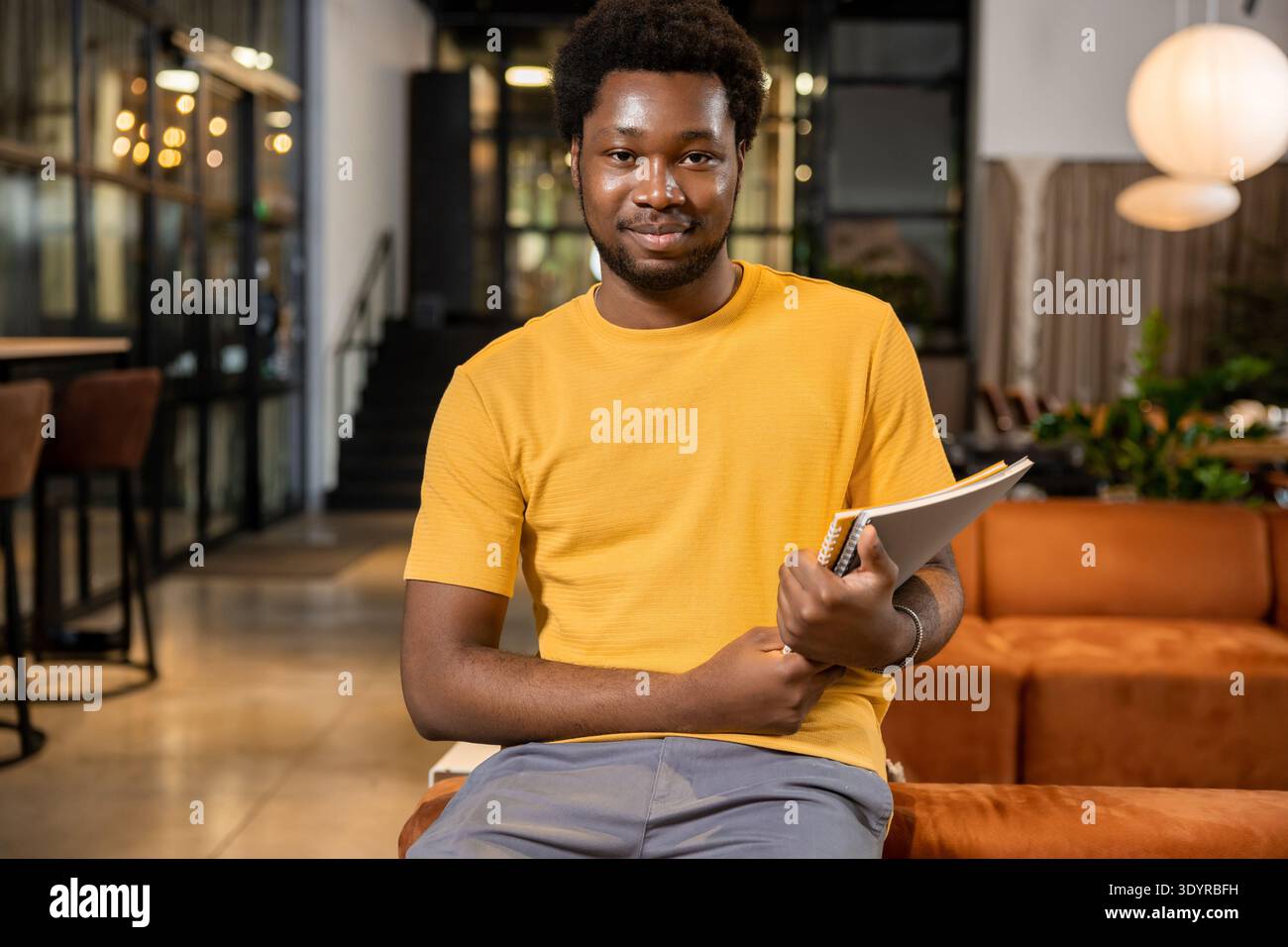 Uomo sicuro di sé che riposa sul divano con blocco note sorridente in un ambiente di coworking Foto Stock
