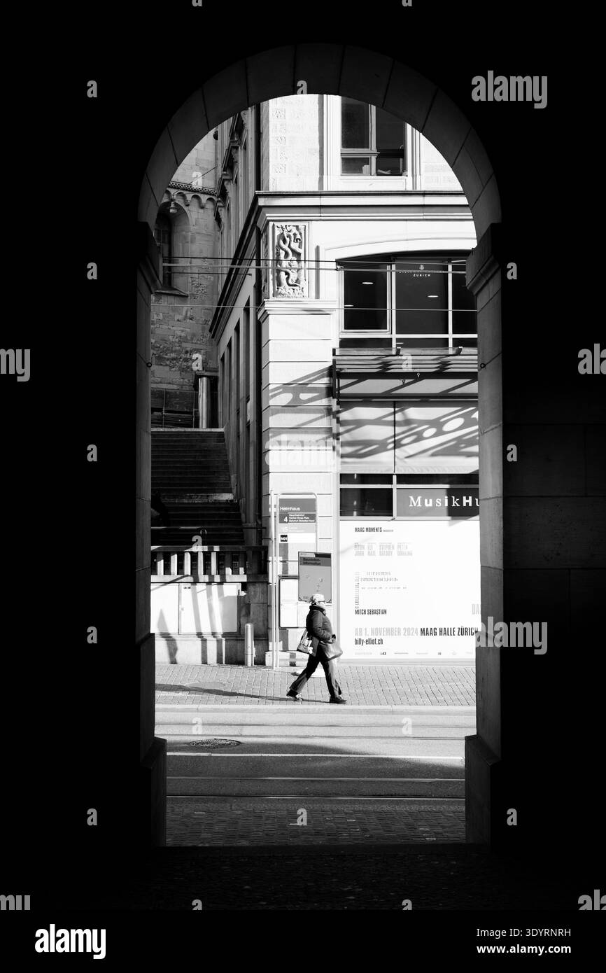 Scena di strada bianca e nera incorniciata da un arco, che mostra una persona che cammina in un ambiente urbano con dettagli architettonici e composizioni forti Foto Stock