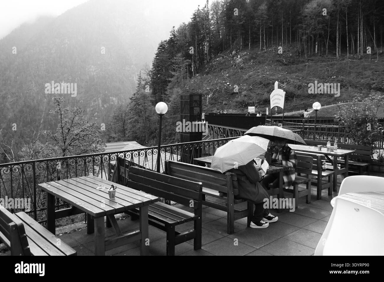 Persone sedute sotto gli ombrelloni in una terrazza all'aperto durante le piogge in un paesaggio montuoso, creando un momento tranquillo e suggestivo in natura Foto Stock