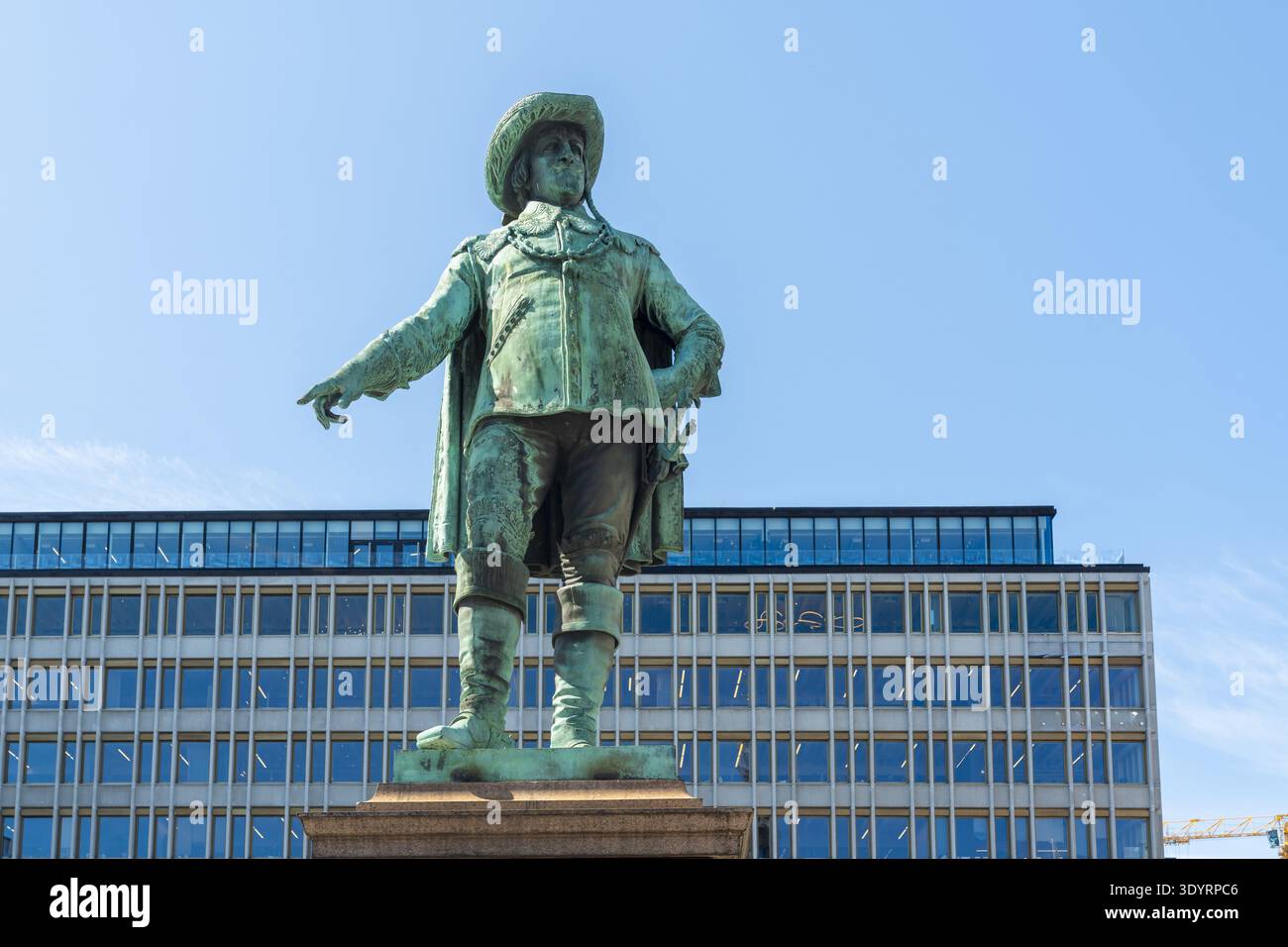 La vista di una statua cristiana IV ricoperta di verdigri, raffigurante un uomo in abito d'epoca, si erge in modo sfacciato su uno sfondo di moderna architettura in vetro sotto un cle Foto Stock
