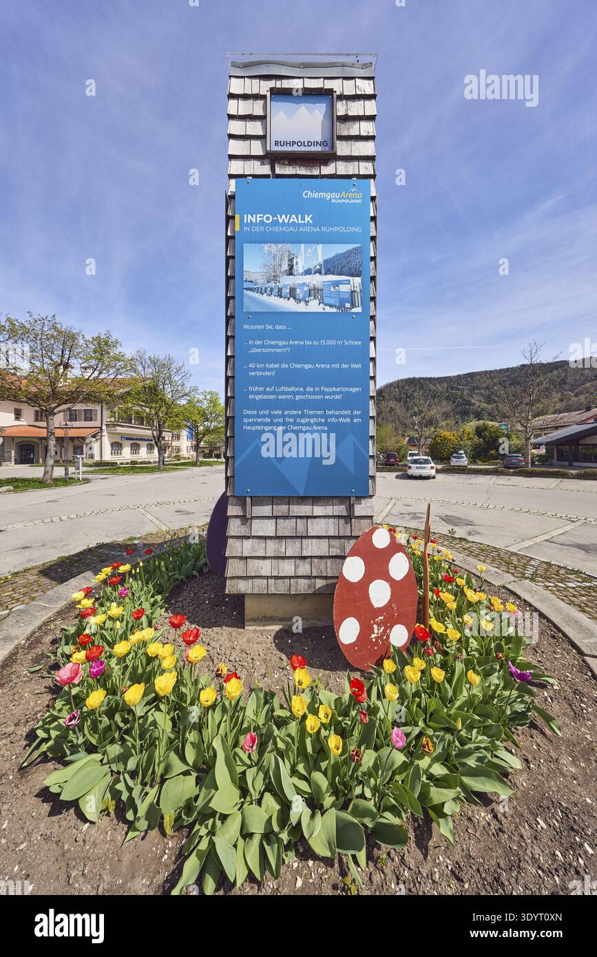 Stele con informazioni turistiche sulla Chiemgau Arena Ruhpolding, aiuole rotonde, decorazioni pasquali, parcheggio con auto, architettura generale, Foto Stock