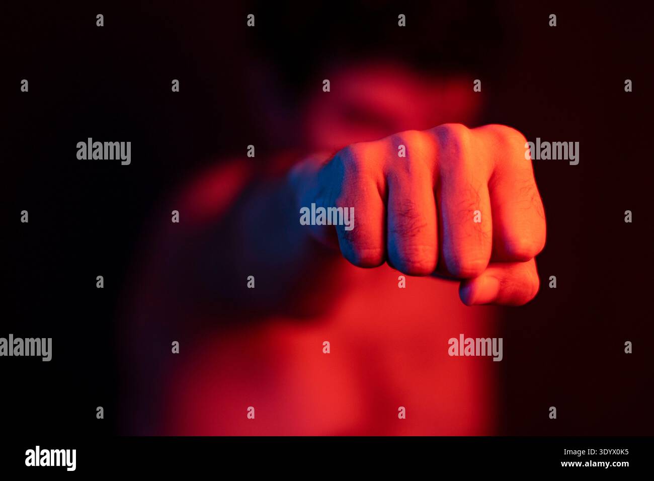Uomo arrabbiato che pugni, pugile, allenamento con sfondo sfocato. Uomo violento che pugni, picchia. Luci rosse, violenza. Foto Stock