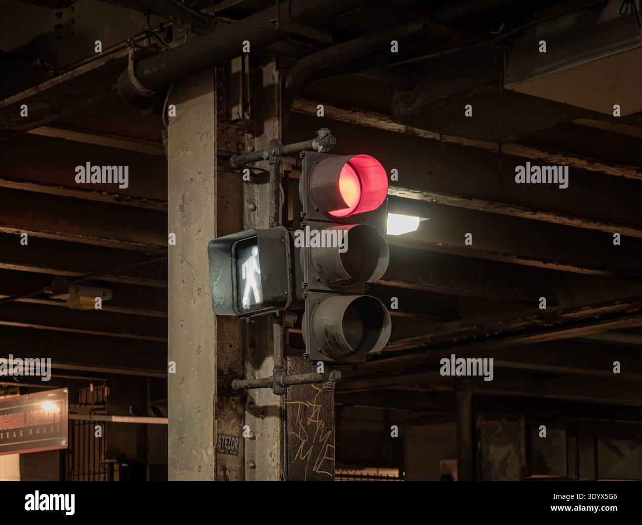 Il semaforo rosso e il segnale di passeggiata pedonale sono illuminati di notte sotto una grintosa struttura di ponti urbani nel centro di Chicago Foto Stock