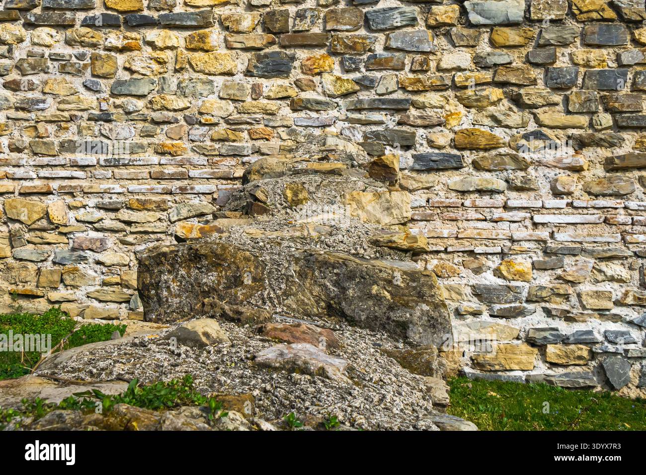Pareti in pietra intemperie costruite con rocce irregolari con resti di una vecchia struttura davanti, che mostrano dettagliate strutture murarie in un'architettura storica Foto Stock