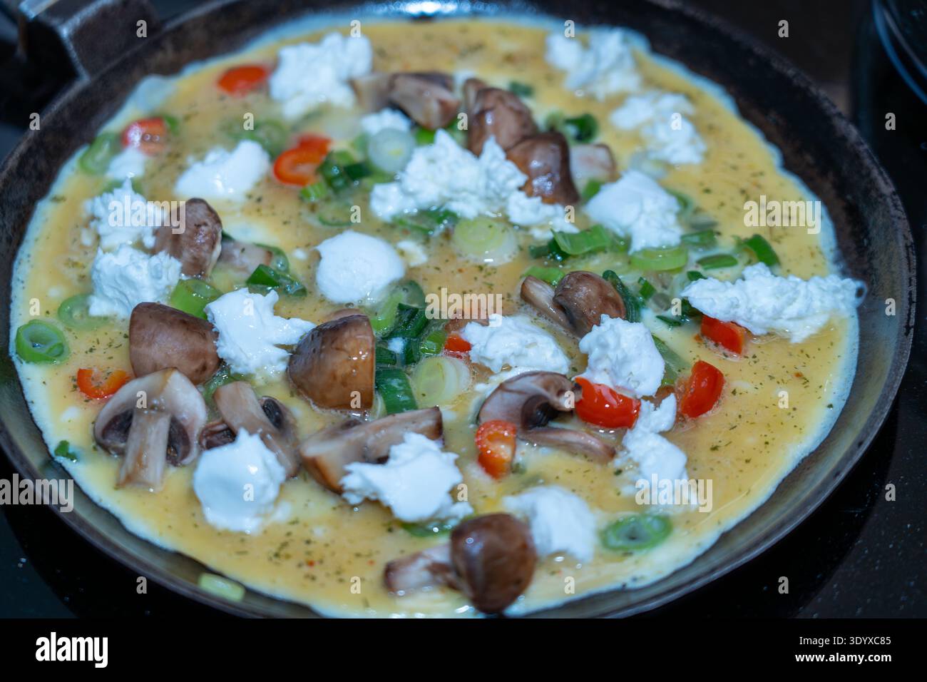 Primo piano con angolo superiore di una frittata all'uovo ricca di proteine, ricoperta da formaggio bianco, funghi e peperoni, che cuoce su una stufa a induzione. Foto Stock