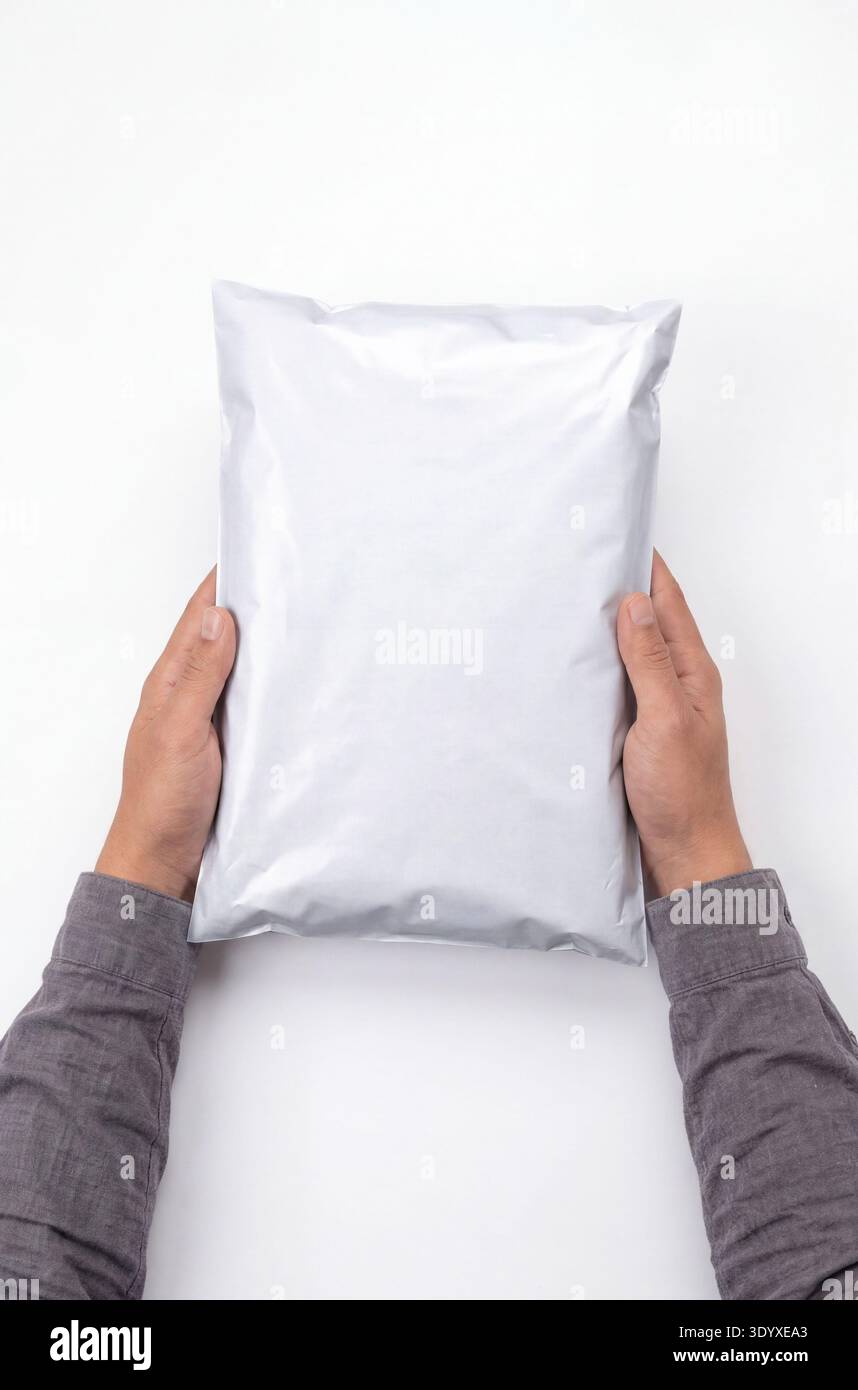 Mockup di un sacchetto per posta in polietilene bianco tenuto da entrambe le mani, isolato su uno sfondo bianco. Foto Stock