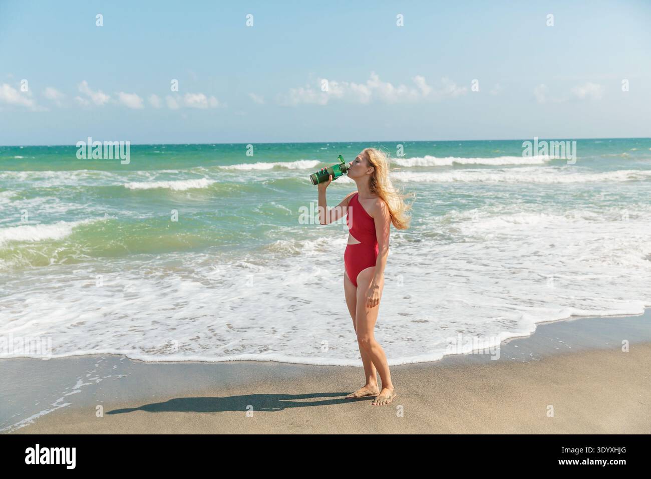 Giovane donna in costume da bagno rosso che tiene in mano una bottiglia d'acqua a Sunny Beach Foto Stock