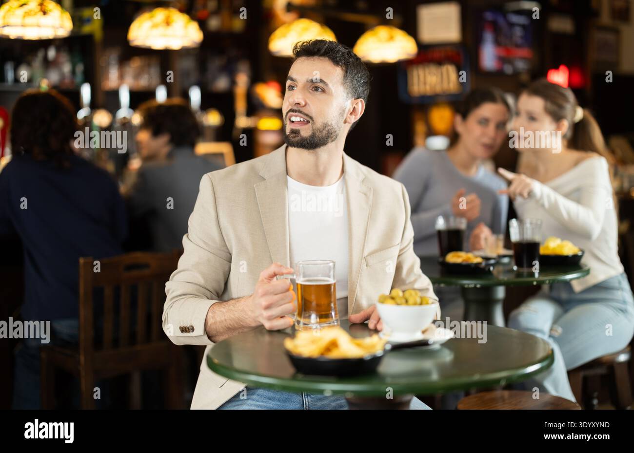 Giovane ragazzo positivo che si rilassa a tavola e beve birra nel pub sportivo, guardando attentamente la partita in TV Foto Stock