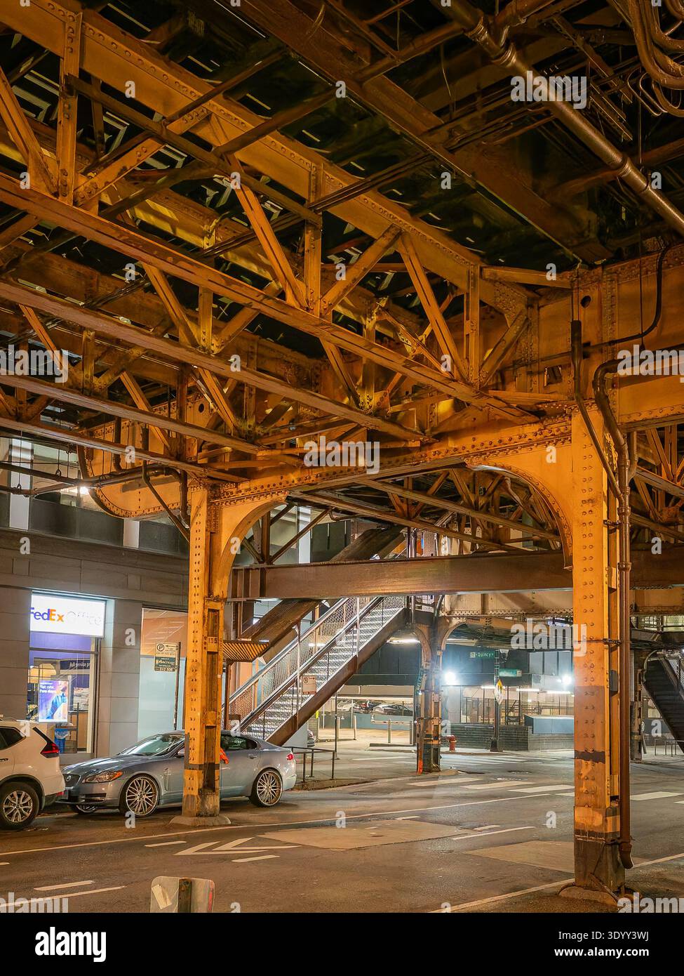 Vista ad angolo basso dell'intricato traliccio in acciaio e della struttura di supporto dei binari sopraelevati di Chicago "l'" di notte sopra una strada della città Foto Stock