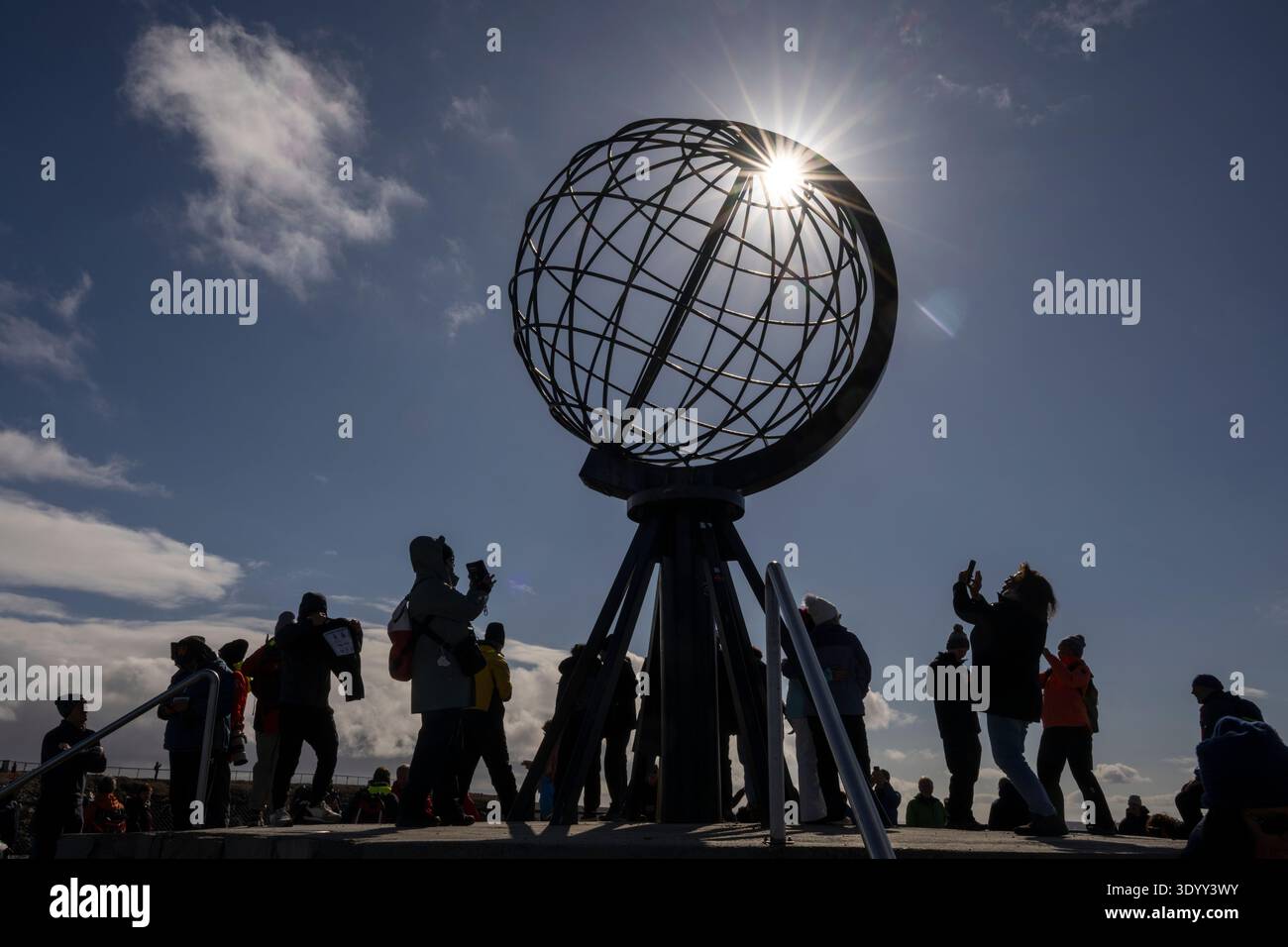 Fotografia retroilluminata con effetto stella che mostra le sagome dei visitatori della sempre popolare scultura a globo a Capo Nord (Nordkapp) sull'isla Foto Stock