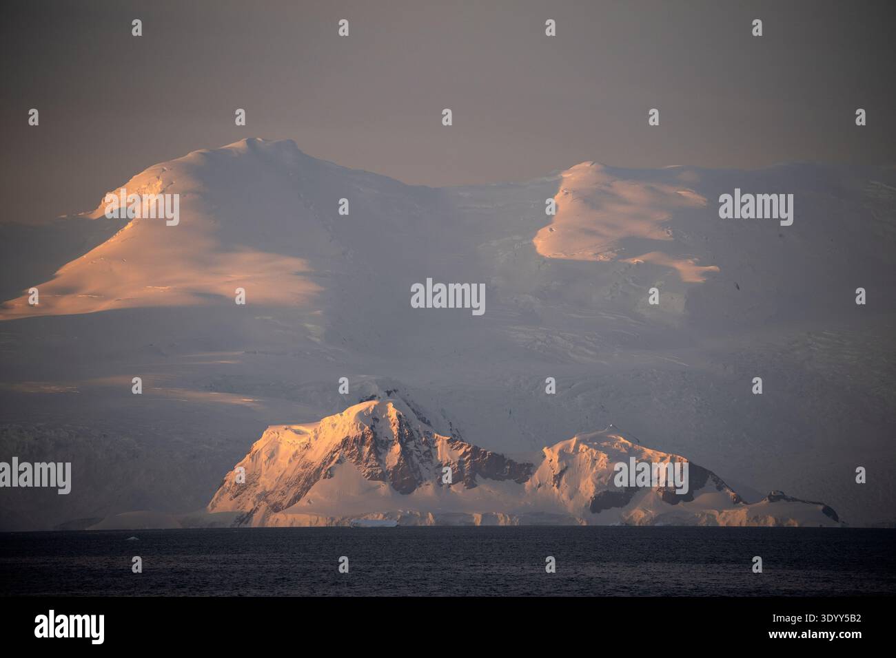 Vista pittoresca alla luce del tardo pomeriggio di un terreno innevato sullo sfondo di alte montagne innevate, Portal Point, Antartico PE Foto Stock