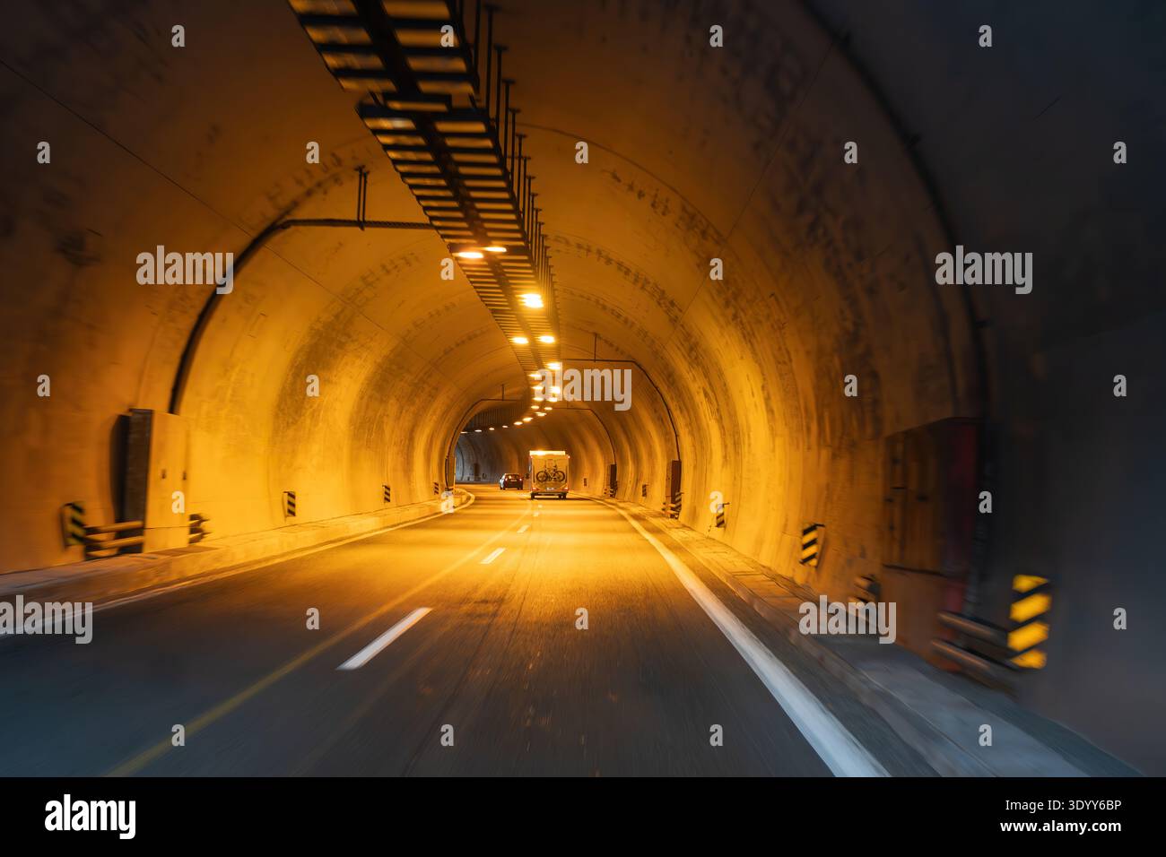 Un veicolo viaggia all'interno di un tunnel al crepuscolo. Le pareti si illuminano di luce calda. La strada è libera e dritta. L'atmosfera sembra chiusa e concentrata Foto Stock