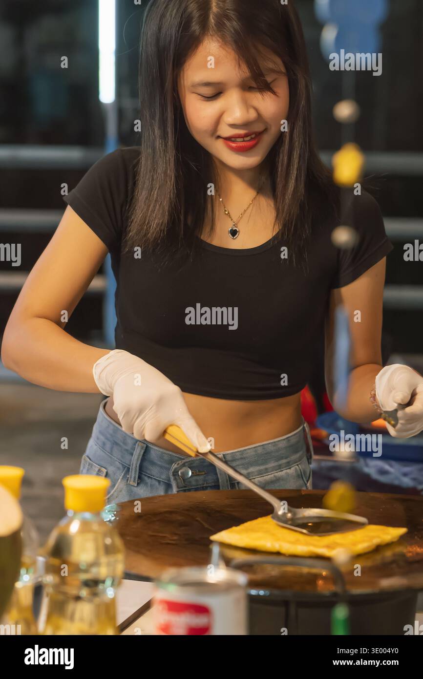 Phuket Thailandia 23 11 2025: Donna che cucina roti dolci in una bancarella di Bangkok, Thailandia, mentre interagisce con i clienti e mostra la tradizione Foto Stock
