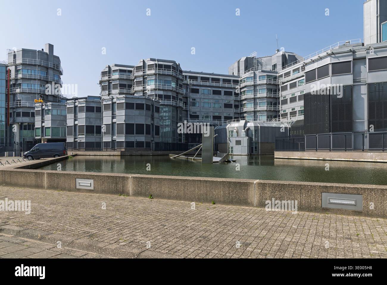 Moderno complesso per uffici in metallo argento dell'AIVD a Zoetermeer con fossato circostante e laghetto riflettente sotto un cielo azzurro limpido in estate. Zoeterme Foto Stock