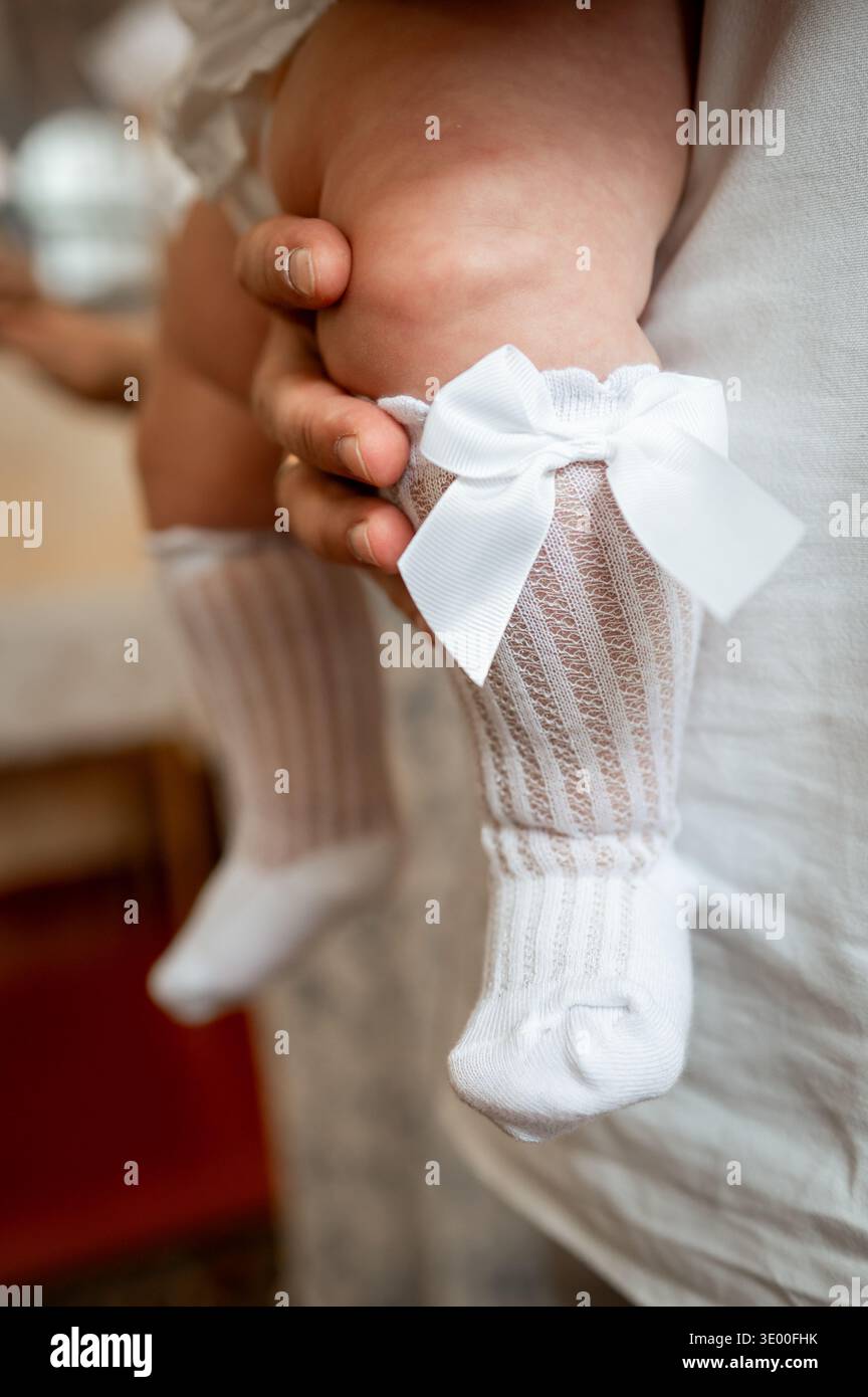 Tenero momento di gambe per neonati che indossano calze al ginocchio decorative in stile vintage e un abito bianco, immagine concettuale dell'innocenza dell'infanzia, moda da festa e Foto Stock