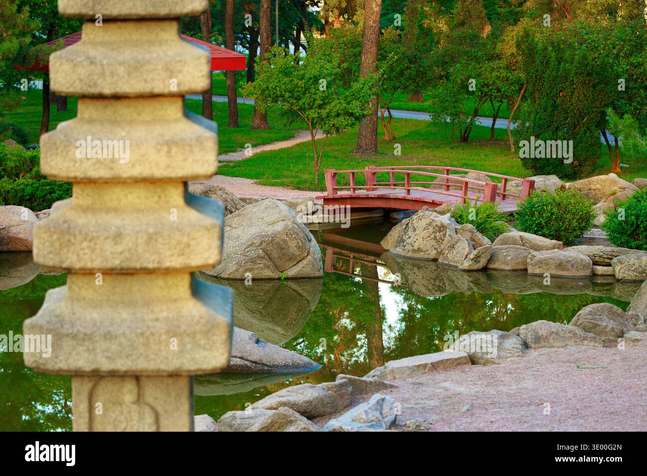 Scoprite la serena bellezza di un giardino giapponese caratterizzato da una lanterna in pietra e da un affascinante ponte in legno Foto Stock