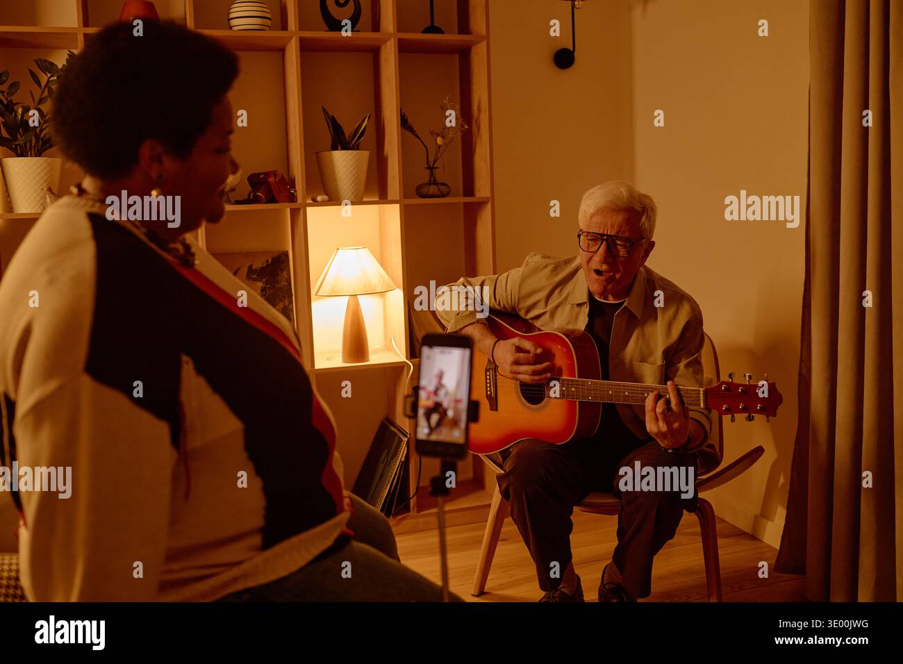 Uomo caucasico senior che suona la chitarra per la donna nera di mezza età a casa Foto Stock