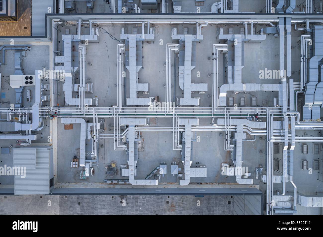 Vista aerea di una rete di condotti e tubi che creano un intricato motivo geometrico su un tetto, un netto contrasto tra precisione industriale e Foto Stock