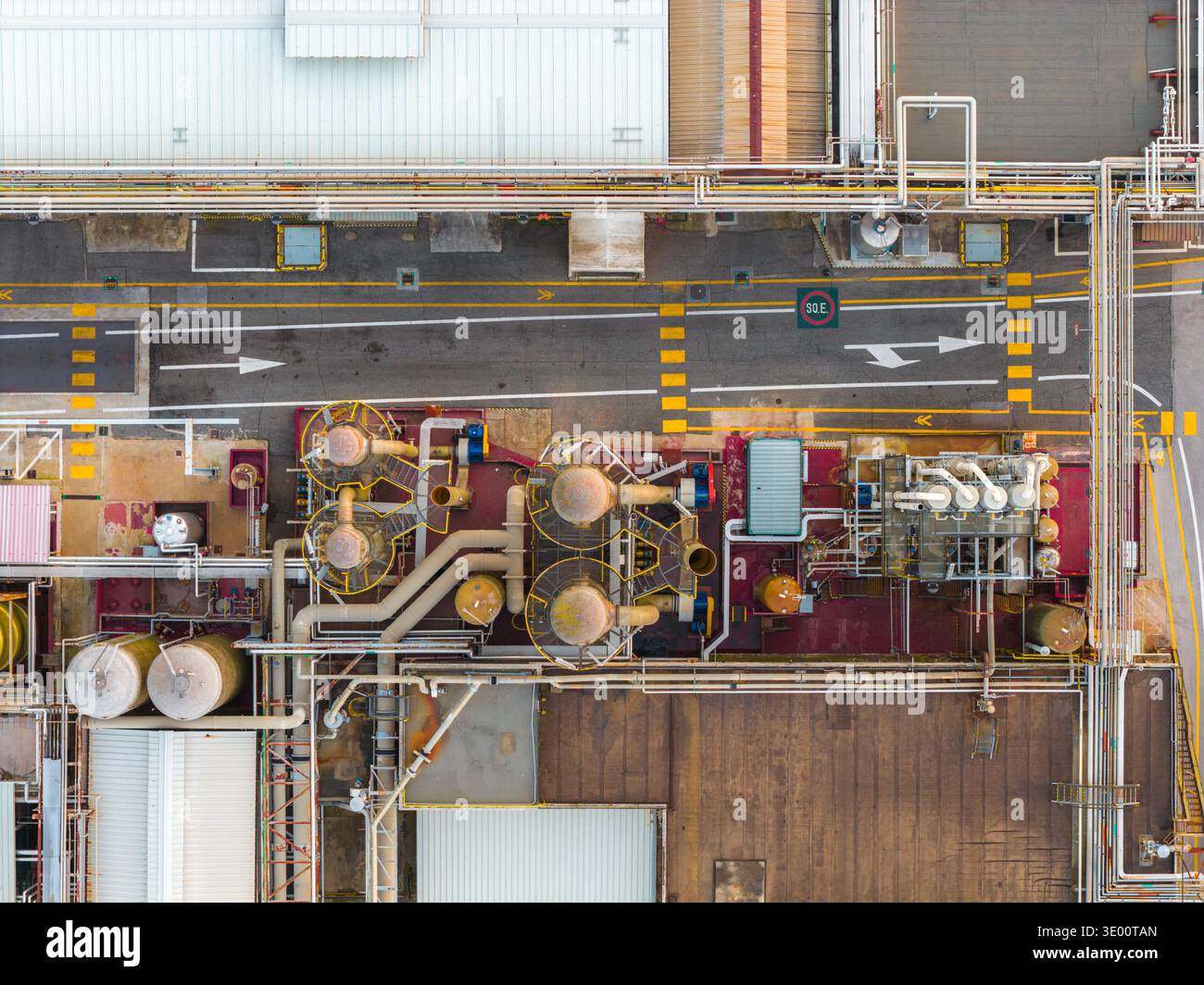 La vista aerea del complesso industriale rivela una rete di tubi e serbatoi, accostati a strade asfaltate, creando un vivace arazzo di texture Foto Stock