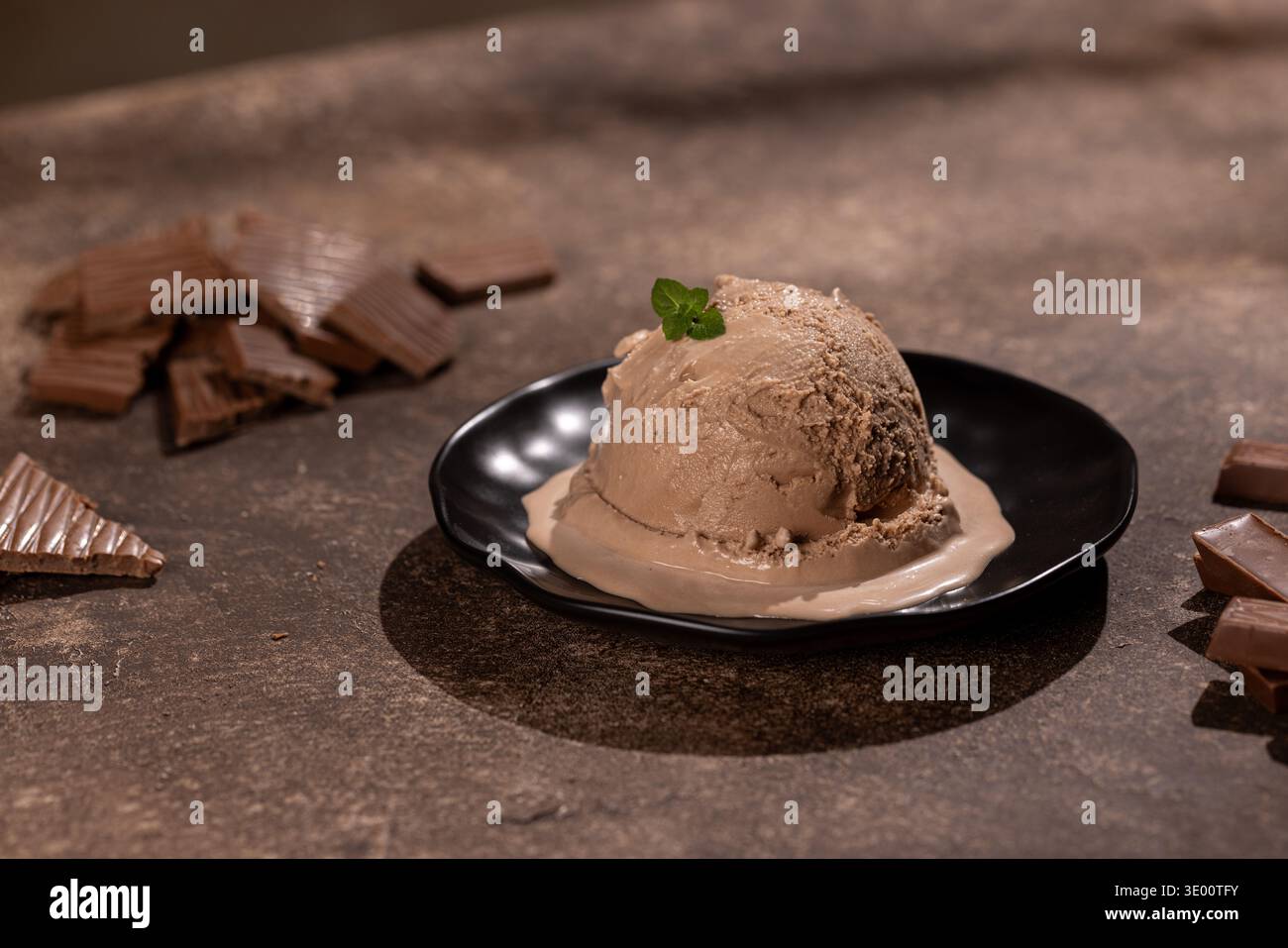 Primo piano di una grande tazza di gelato cremoso al cioccolato, cosparso di scaglie di cioccolato pregiate, su un piatto nero opaco. Lo studio ha girato in guerra Foto Stock