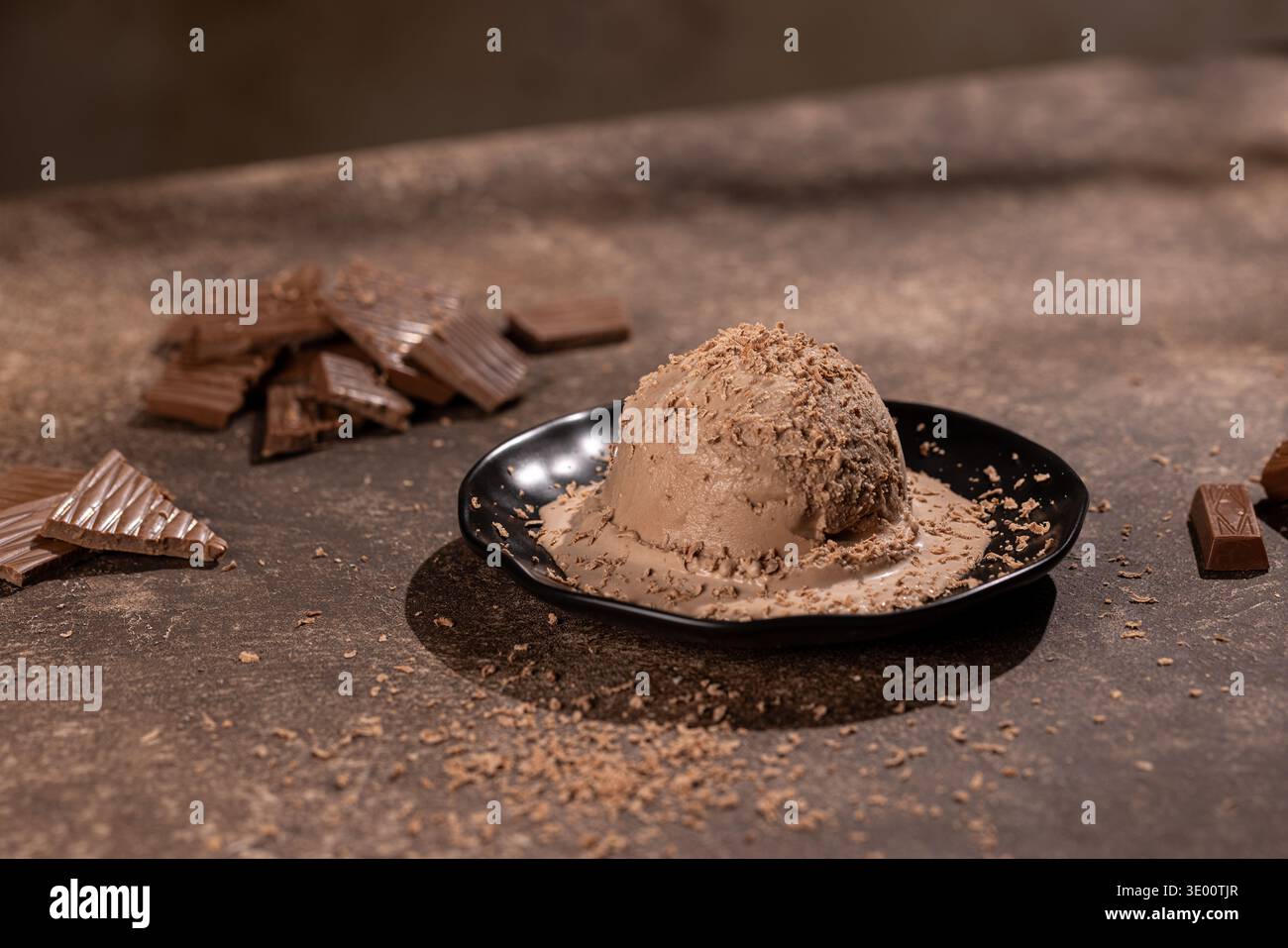 Primo piano di una grande tazza di gelato cremoso al cioccolato, cosparso di scaglie di cioccolato pregiate, su un piatto nero opaco. Lo studio ha girato in guerra Foto Stock