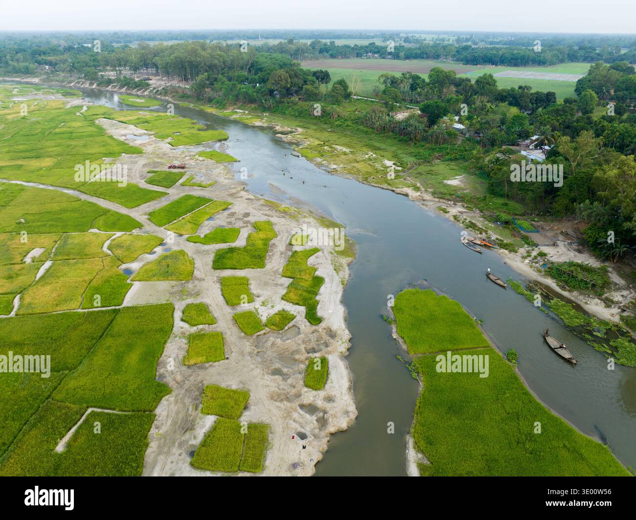 Veduta aerea del fiume sereno e tortuoso che serpeggia tra i vivaci campi verdi e le macchie sabbiose sotto un cielo morbido e coperto, Tetulia, Rangpur Division, Foto Stock