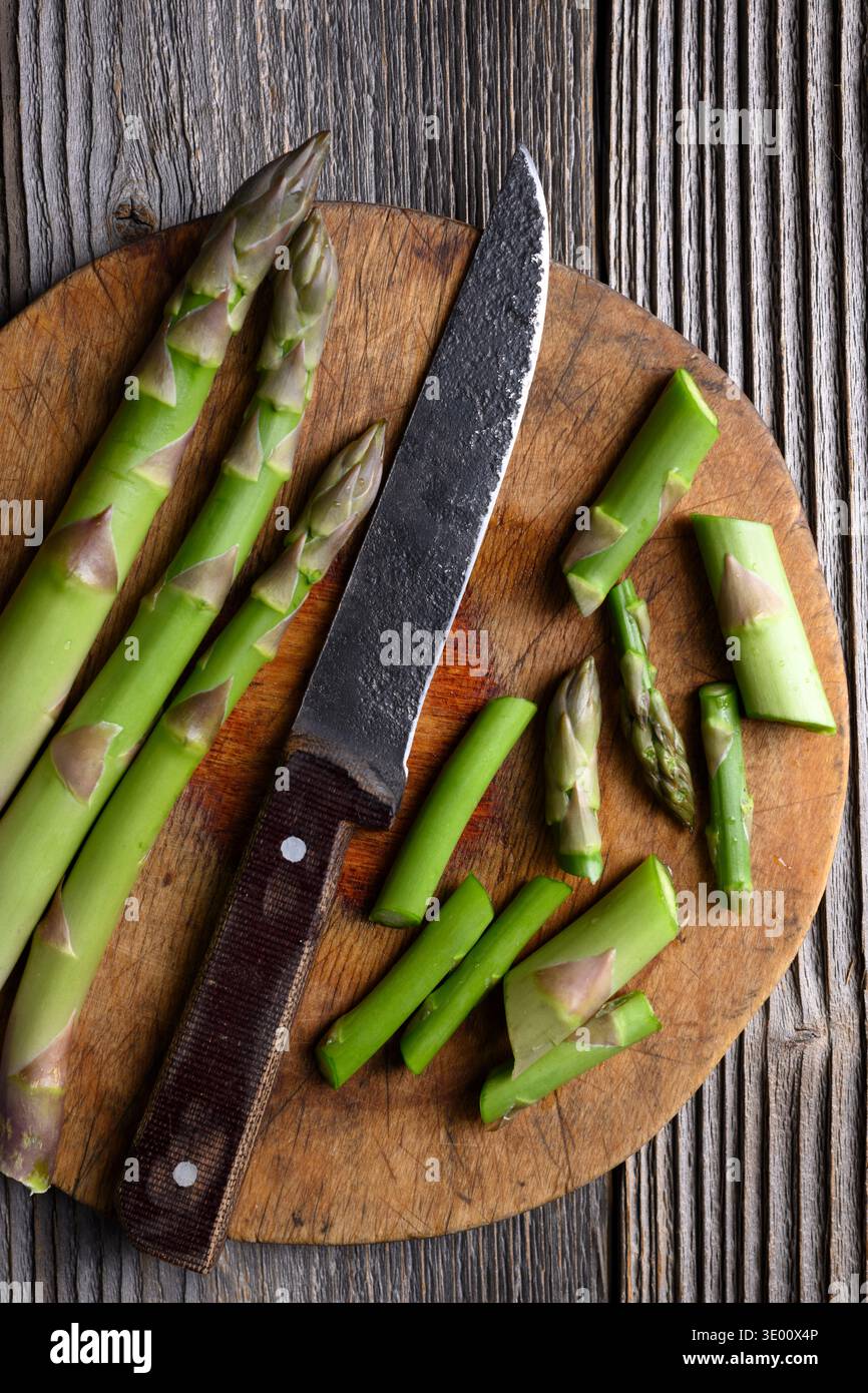 Asparagi verdi a fette disposti su un tagliere in legno rustico. Verdure di stagione crude in background alimentare naturale. Disposizione piatta, vista dall'alto Foto Stock