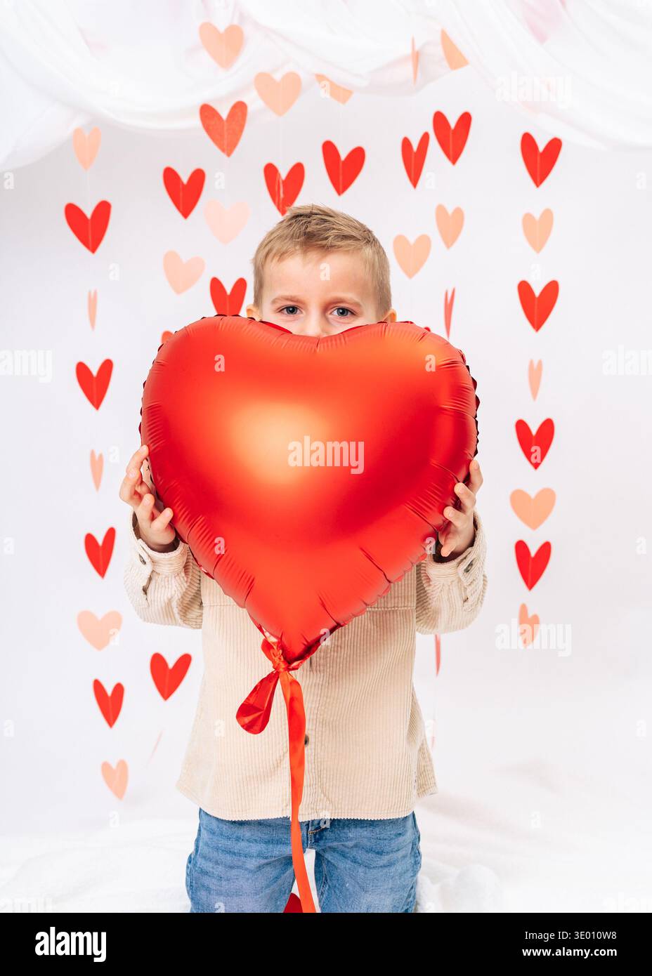 Bambino sorridente che tiene in mano il palloncino rosso con il cuore su sfondo bianco. San Valentino, amore, regalo e festeggiamenti per l'infanzia Foto Stock