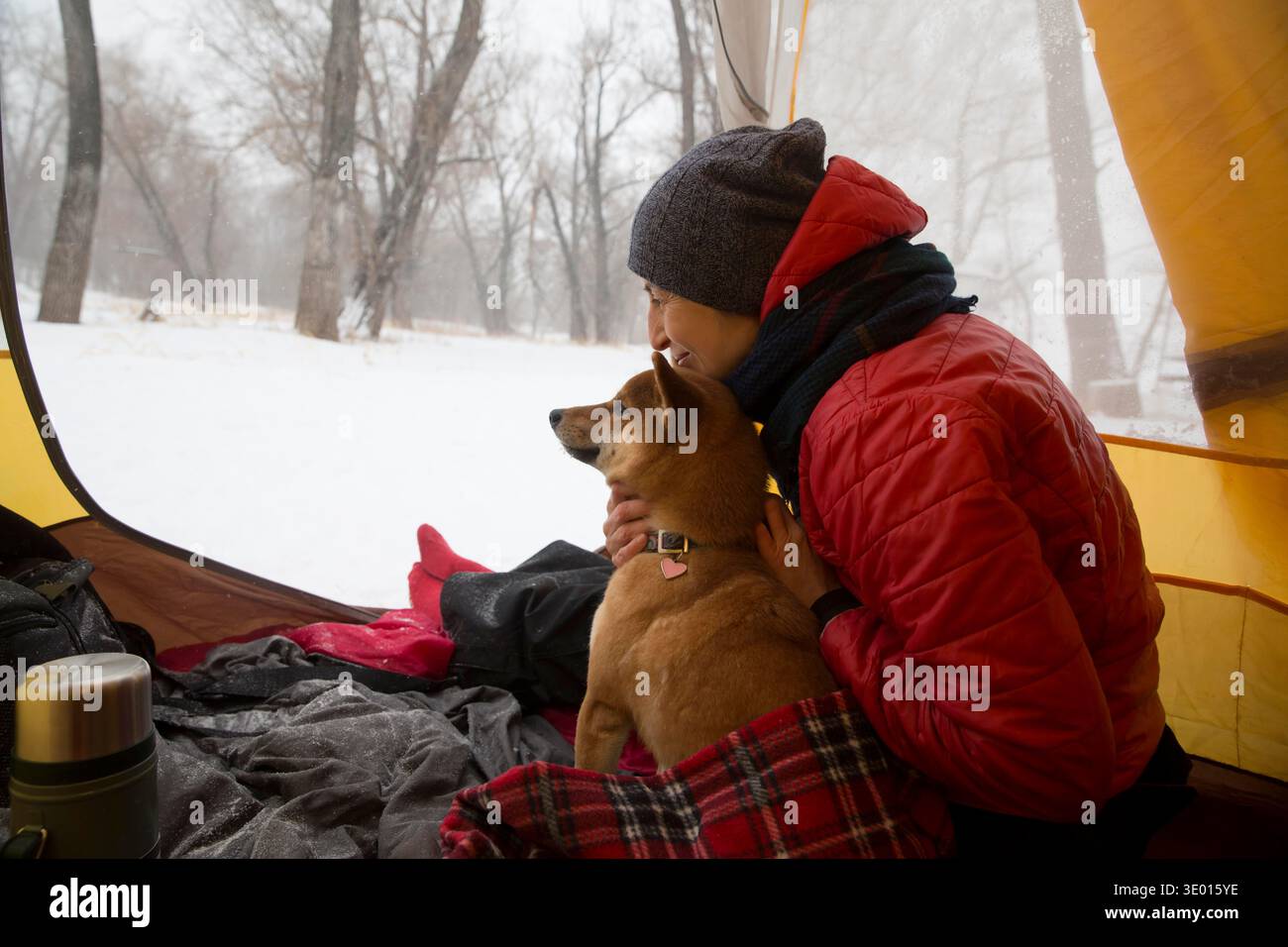 una donna con un cane siede in una tenda durante un'escursione invernale. Distanziamento sociale. Detox digitale. Staycations, viaggi iper-locali, fuga, ambiente naturale || modello rilasciato Foto Stock