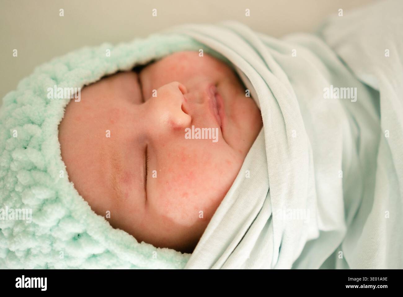 Un neonato avvolto in un morbido panno verde che incarna pacificamente l'innocenza e la tenerezza della prima infanzia e il calore di un ambiente amorevole Foto Stock