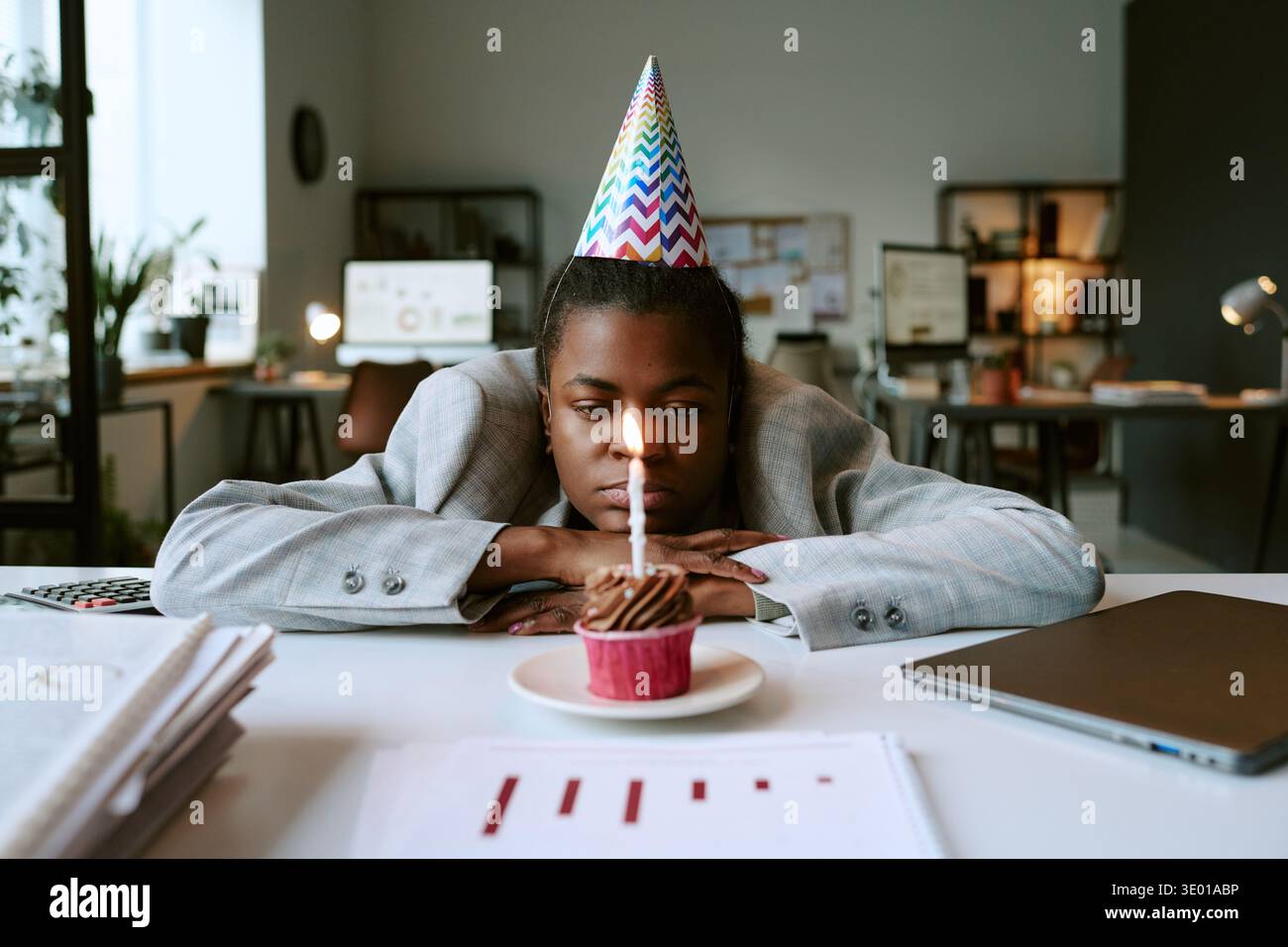 Giovane donna nera adulta che indossa il cappello da festa che fissa la torta di compleanno illuminata Foto Stock