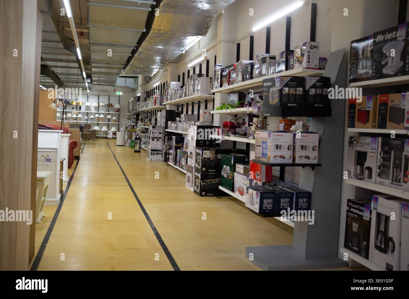 Pforzheim Germania 9 marzo 2026 Long Perspective Electronics Aisle con canaline a soffitto visibili e contrassegnati Yellow Floor Endless Rows of Boxed Products A. Foto Stock