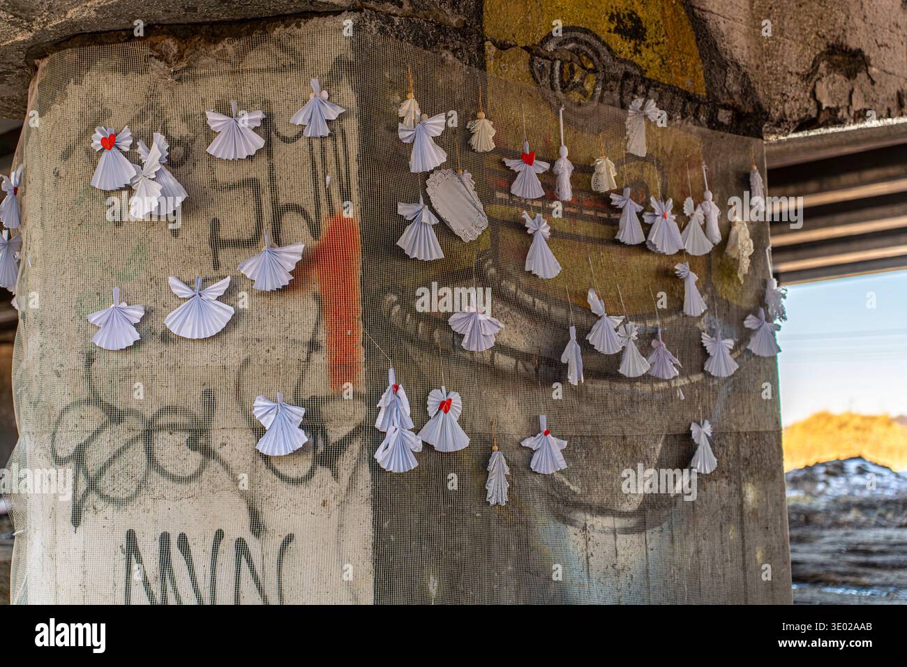 Irpin, Ucraina - 07 marzo 2026: Vista di angeli di carta che adornano un supporto ponte in cemento, un contrasto commovente con lo sfondo di graffiti e urba Foto Stock