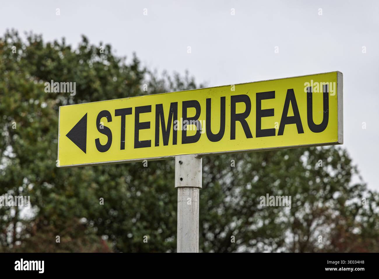 Insegna gialla dei seggi olandesi con testo nero Stembureau su uno sfondo di alberi verdi e un cielo coperto. Foto Stock