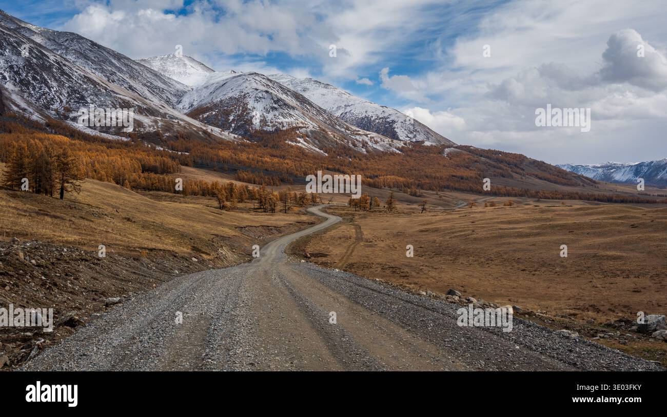 Strada sterrata che si snoda attraverso il bellissimo paesaggio autunnale con montagne innevate e alberi scarsamente sparsi, uno splendido paesaggio naturale Foto Stock