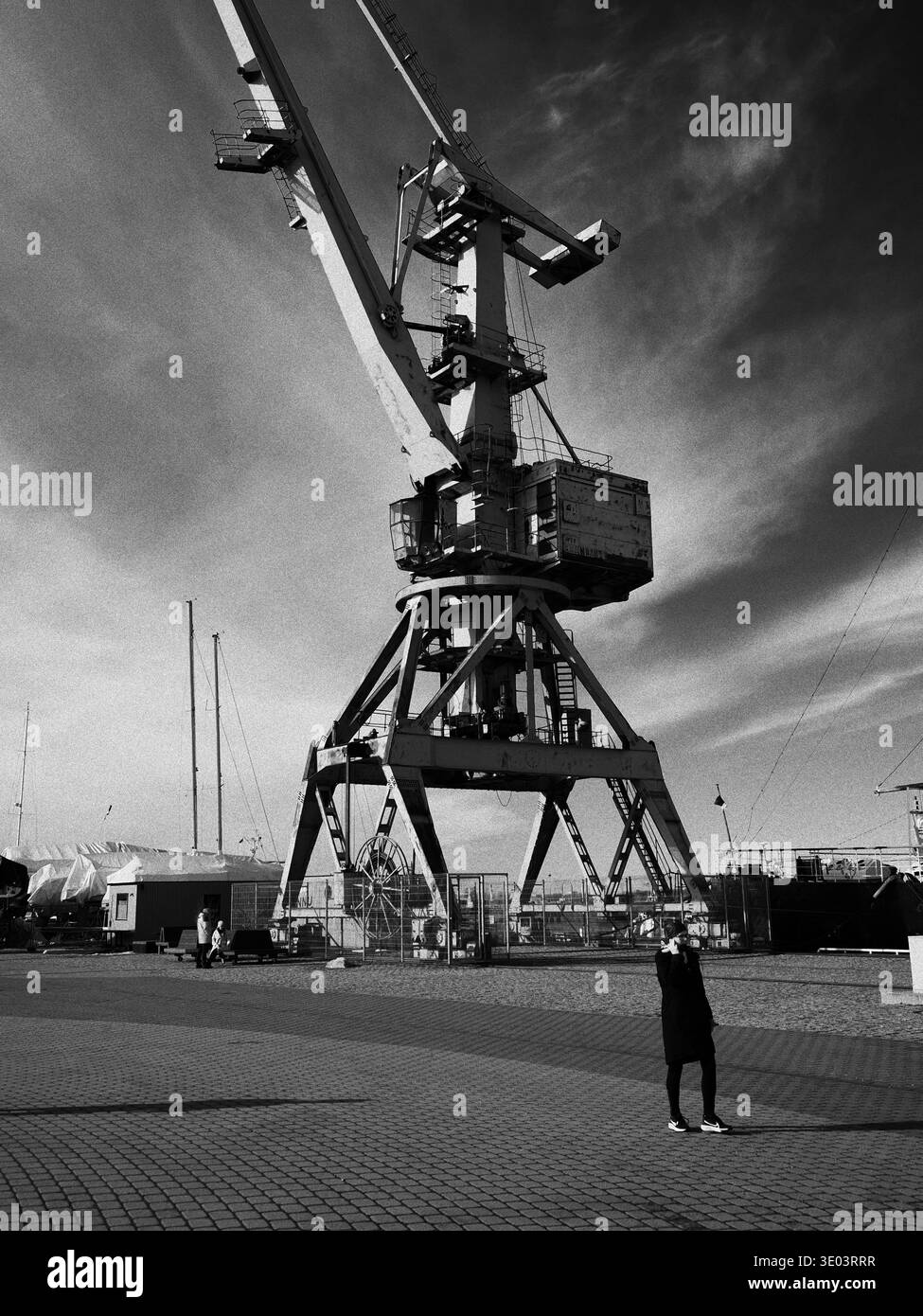Vista in bianco e nero di un'enorme gru portuale industriale che torreggia sopra una persona. Foto Stock