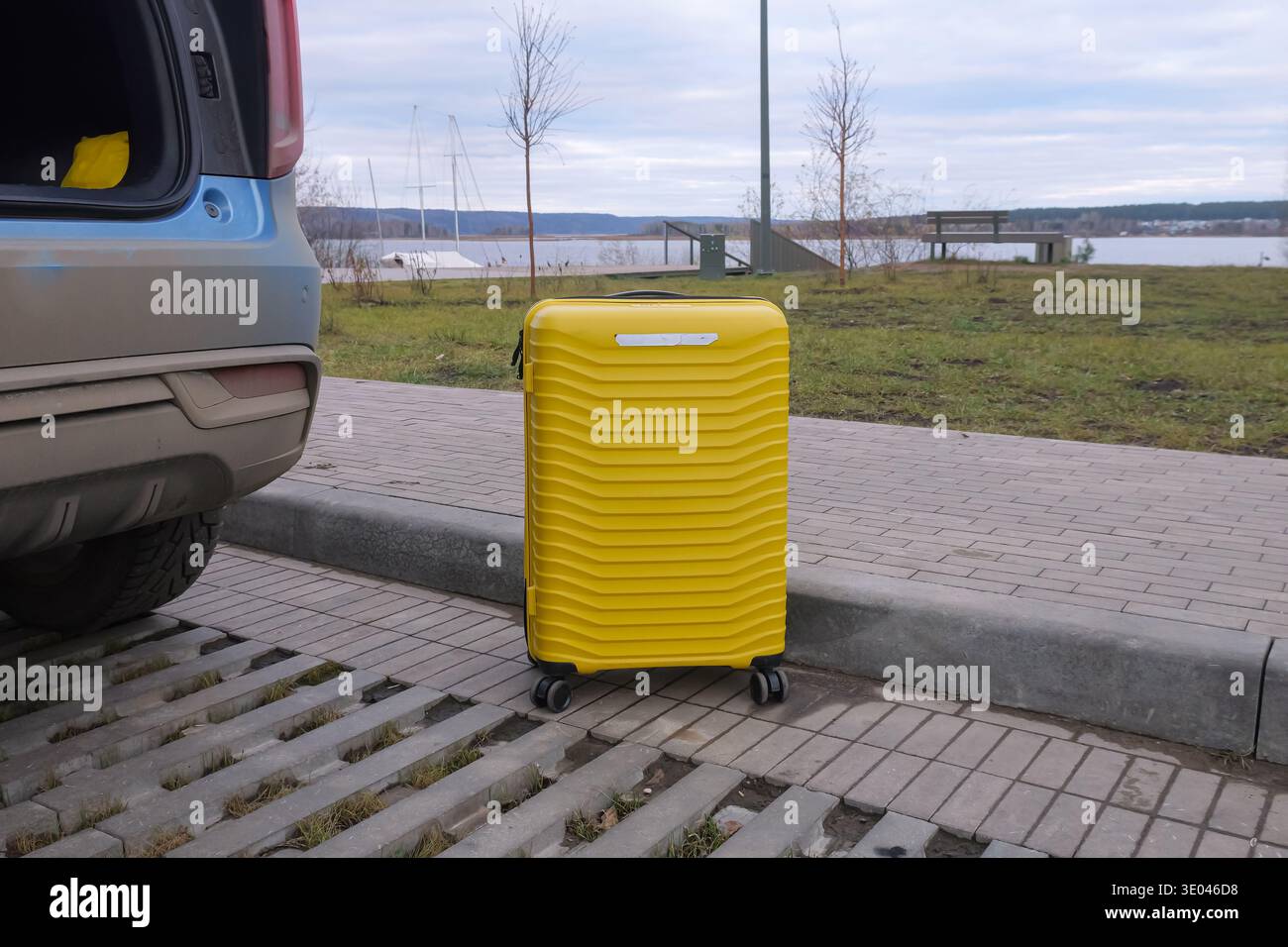 Valigetta gialla da sola sul lato della strada vicino all'acqua sotto il cielo nuvoloso, oggetto da viaggio solitario sul marciapiede ricorda Journey and Independent minimalista Foto Stock