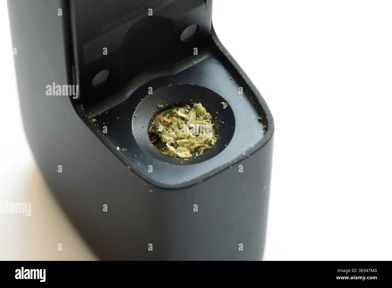 Erba di cannabis caricata in una camera di vaporizzazione secca alle erbe, dettaglio macro del dispositivo nero portatile vape con marijuana macinata, cannabis medica e gamba Foto Stock