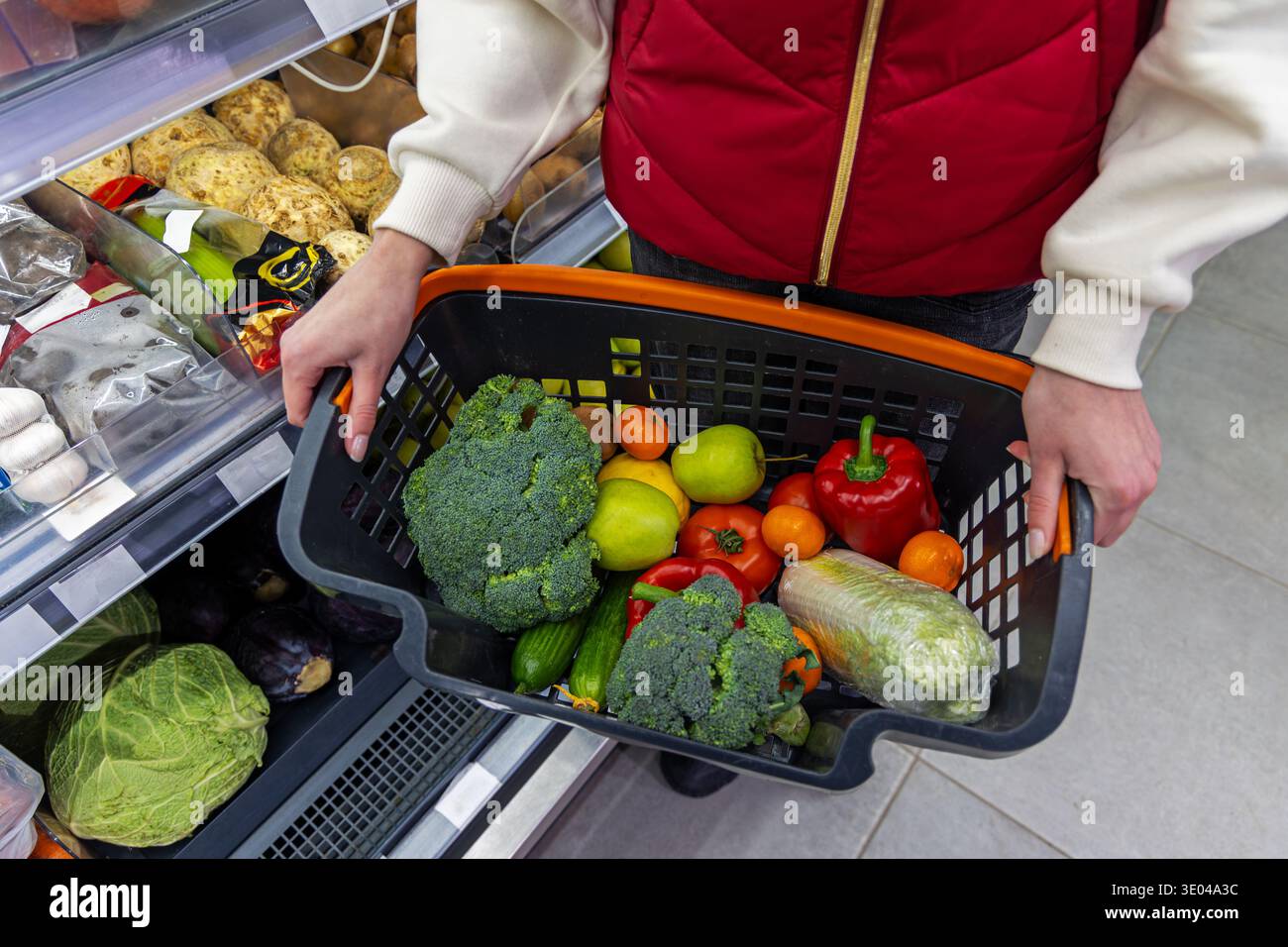 Il cliente trasporta un cestino di prodotti freschi. Un cliente tiene in un supermercato un cestino di alimentari ripieno di frutta e verdura fresca, evidenziando la guarigione Foto Stock