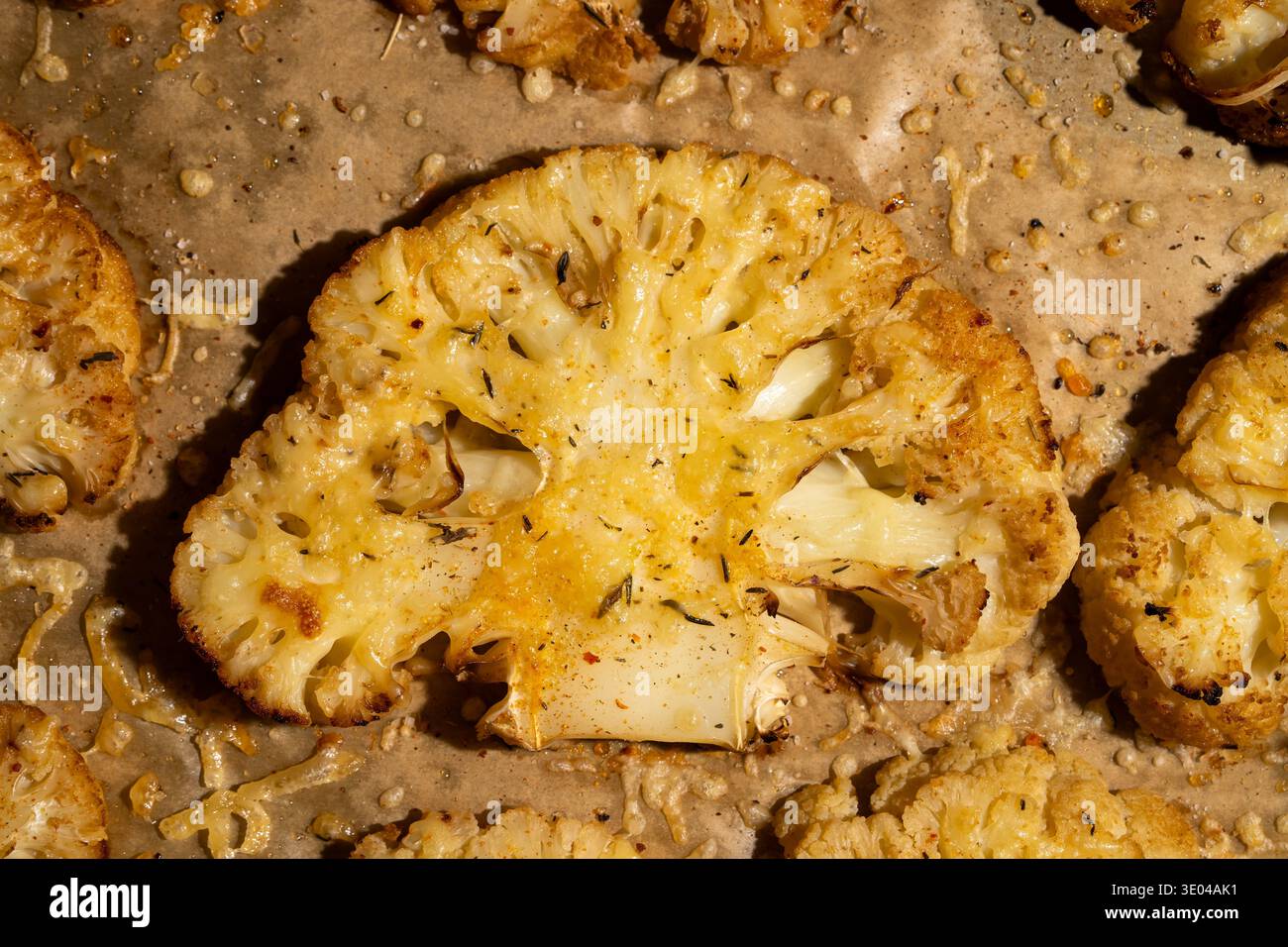 Primo piano di bistecche di cavolfiore arrostite condite con erbe e spezie, disposte su un foglio di carta pergamena, che presenta un piano delizioso e salutare Foto Stock