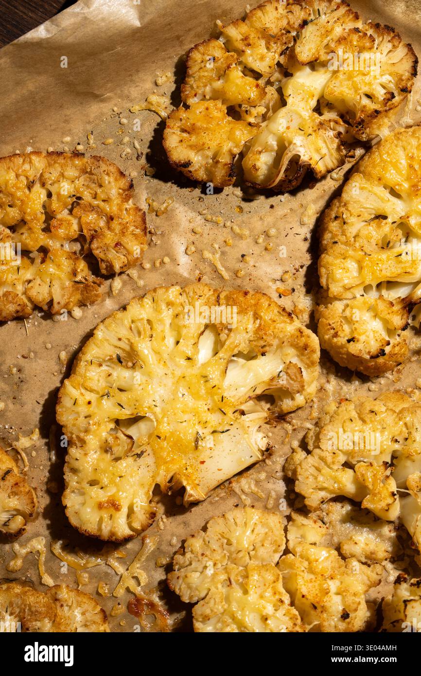 Un primo piano di bistecche di cavolfiore arrostite condite con spezie ed erbe aromatiche su una teglia da forno. Questo piatto sano offre un saporito alternativ a base vegetale Foto Stock