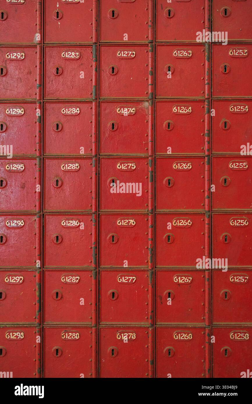 Una raccolta di cassette postali rosse vintage disposte in righe ordinate, ciascuna etichettata con numeri univoci. L'immagine presenta un design classico e vivace e. Foto Stock