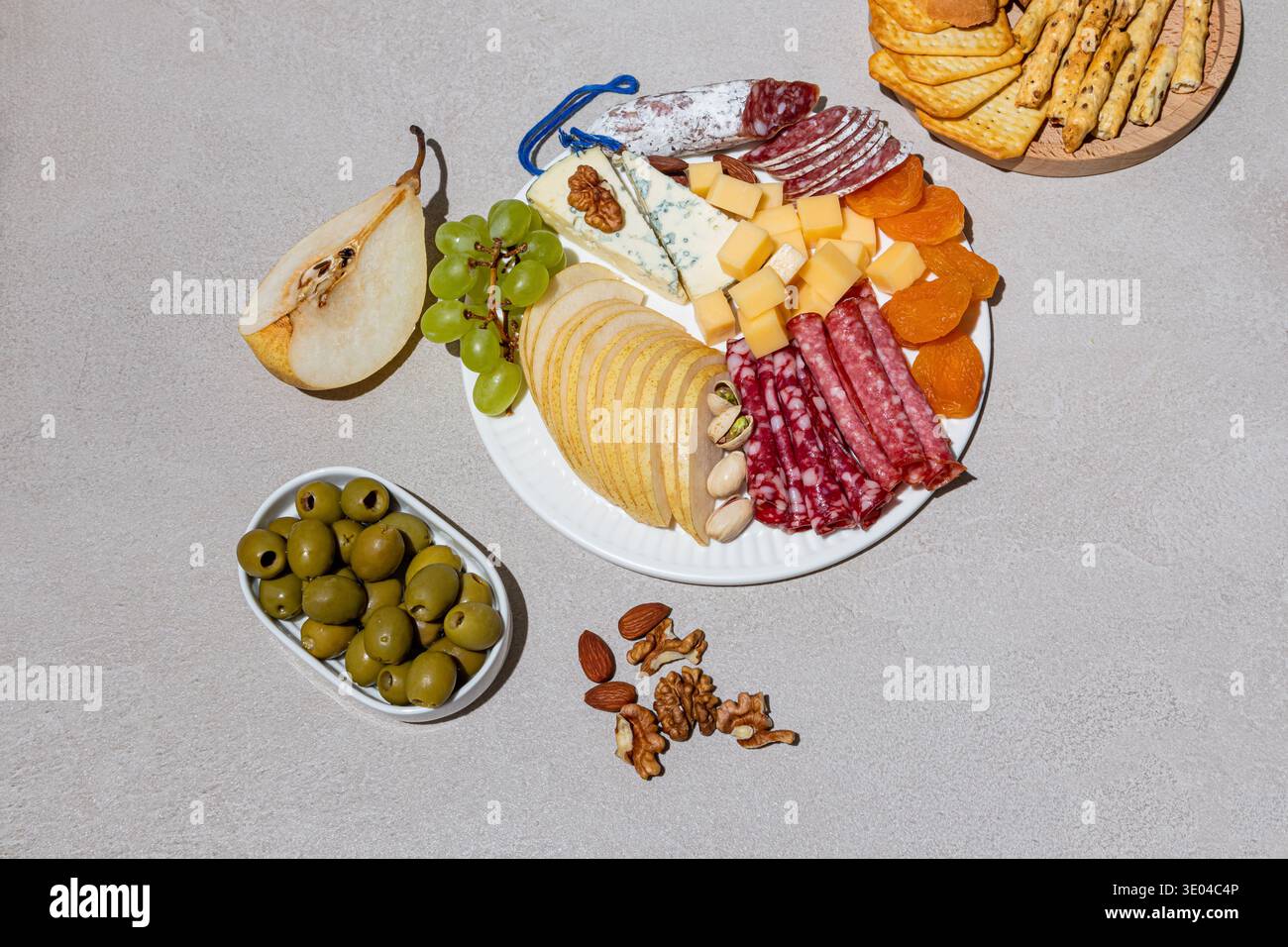 Un elegante vassoio di formaggi con una varietà di formaggi, affettati, frutta fresca e noci disposti ad arte su un piatto bianco, perfetto per intrattenere Foto Stock