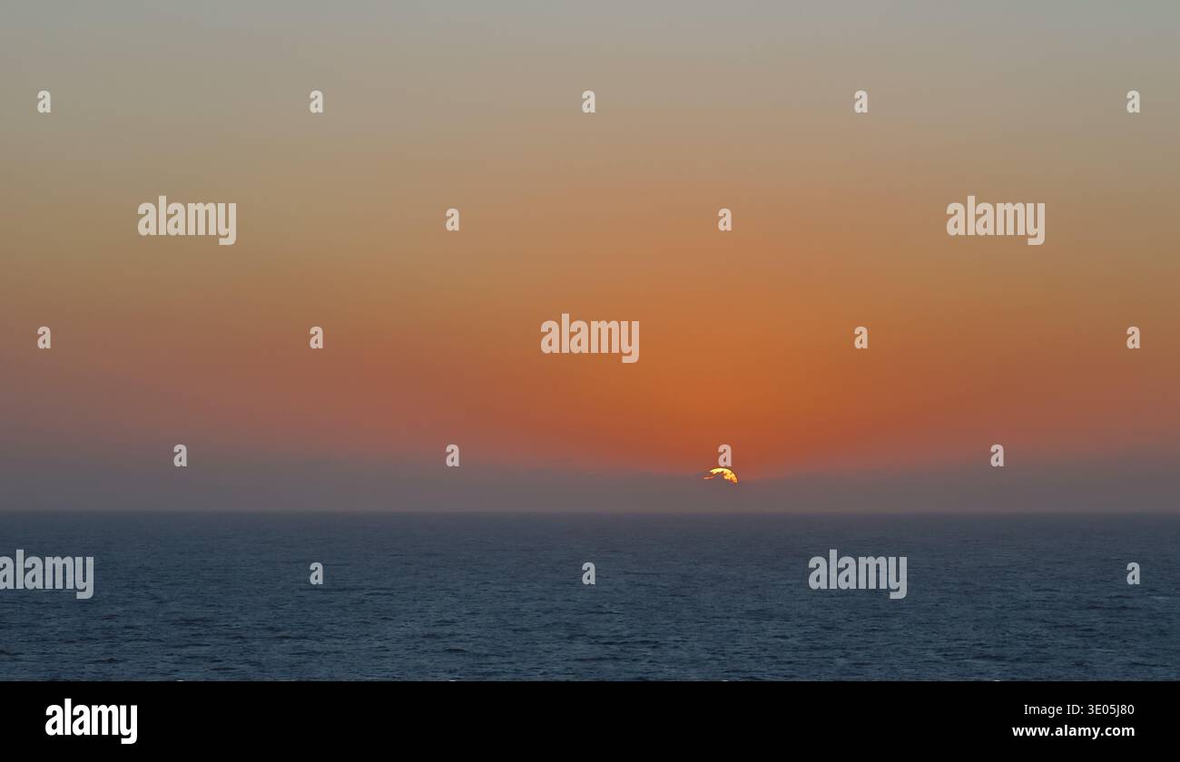 Tramonto sull'orizzonte dell'oceano con caldo cielo arancione e mare calmo che creano un tranquillo paesaggio marino. Foto Stock