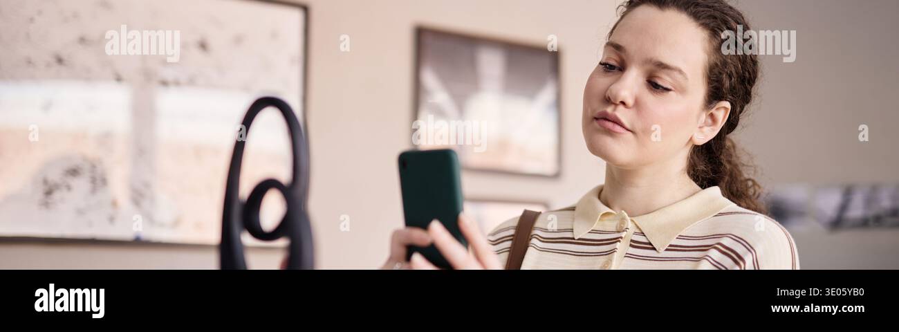 Giovane donna caucasica adulta che fotografa sculture con smartphone in interni Foto Stock