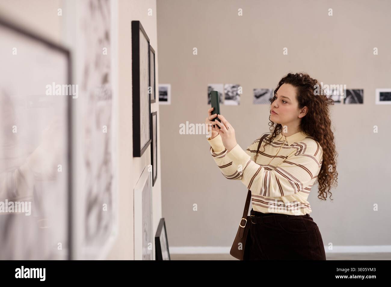Giovane donna caucasica che fotografa opere d'arte durante la visita alla galleria Foto Stock