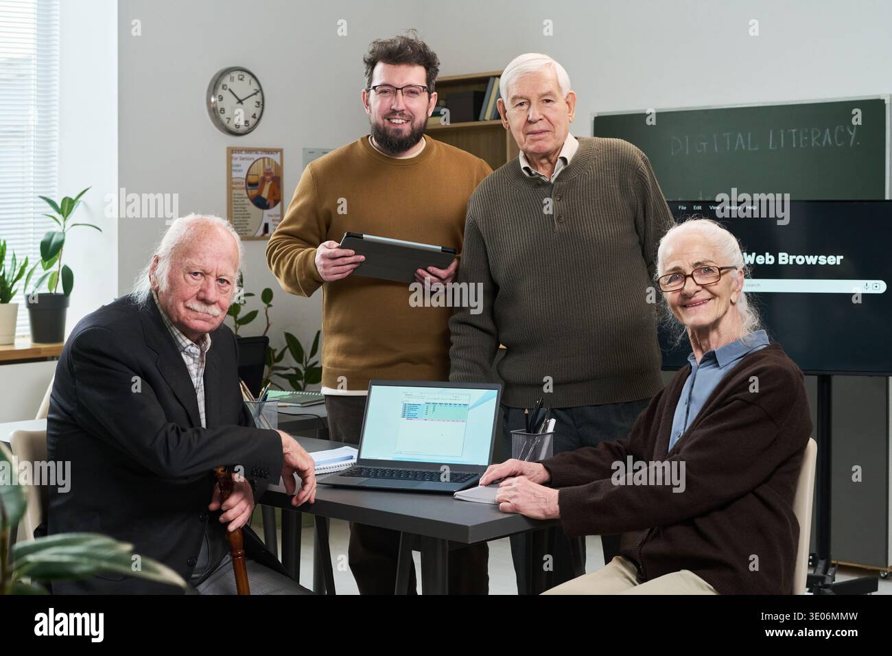 Gruppo di uomo caucasico di mezza età, uomo caucasico anziano, donna caucasica anziana e giovane uomo caucasico adulto che partecipa a un corso di alfabetizzazione informatica utilizzando laptop e tablet in classe Foto Stock