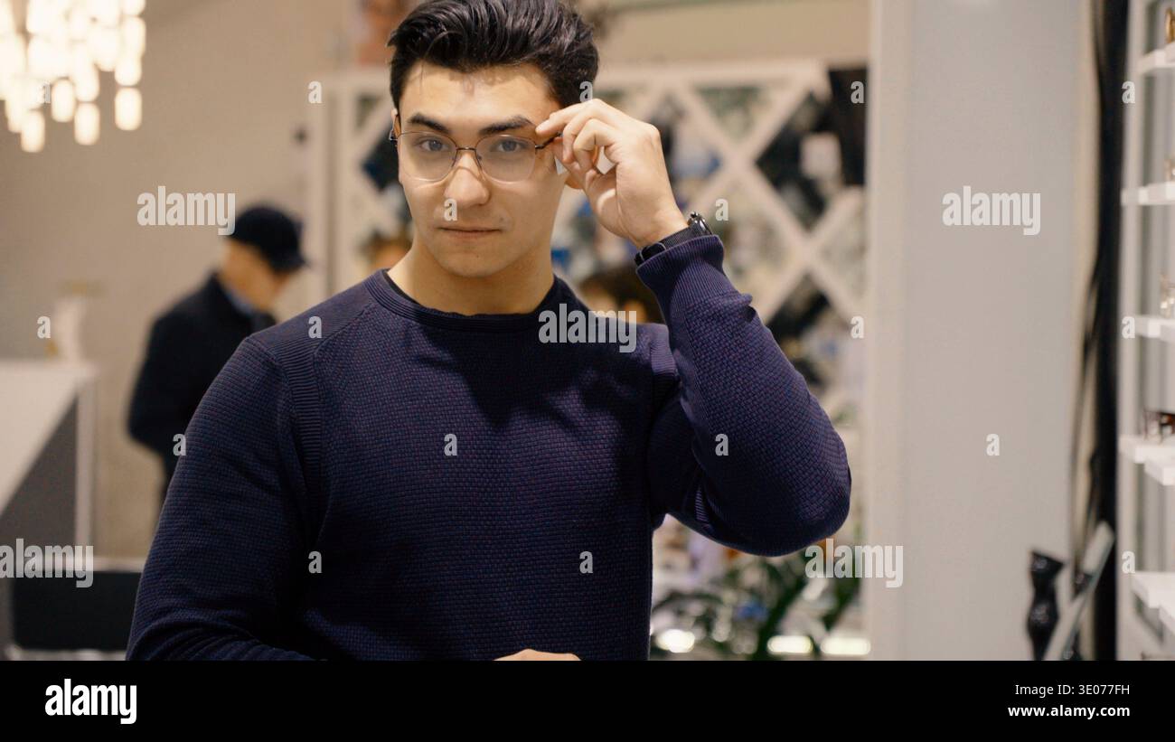 Uomo con maglione scuro che si adatta agli occhiali e sorride Foto Stock