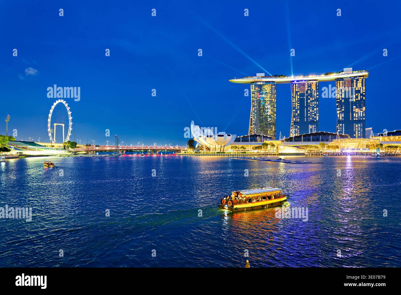 Marina Bay offre una vista dello skyline al tramonto con edifici illuminati. La gente si riunisce per godersi la scena e le luci che si riflettono sull'acqua. Foto Stock