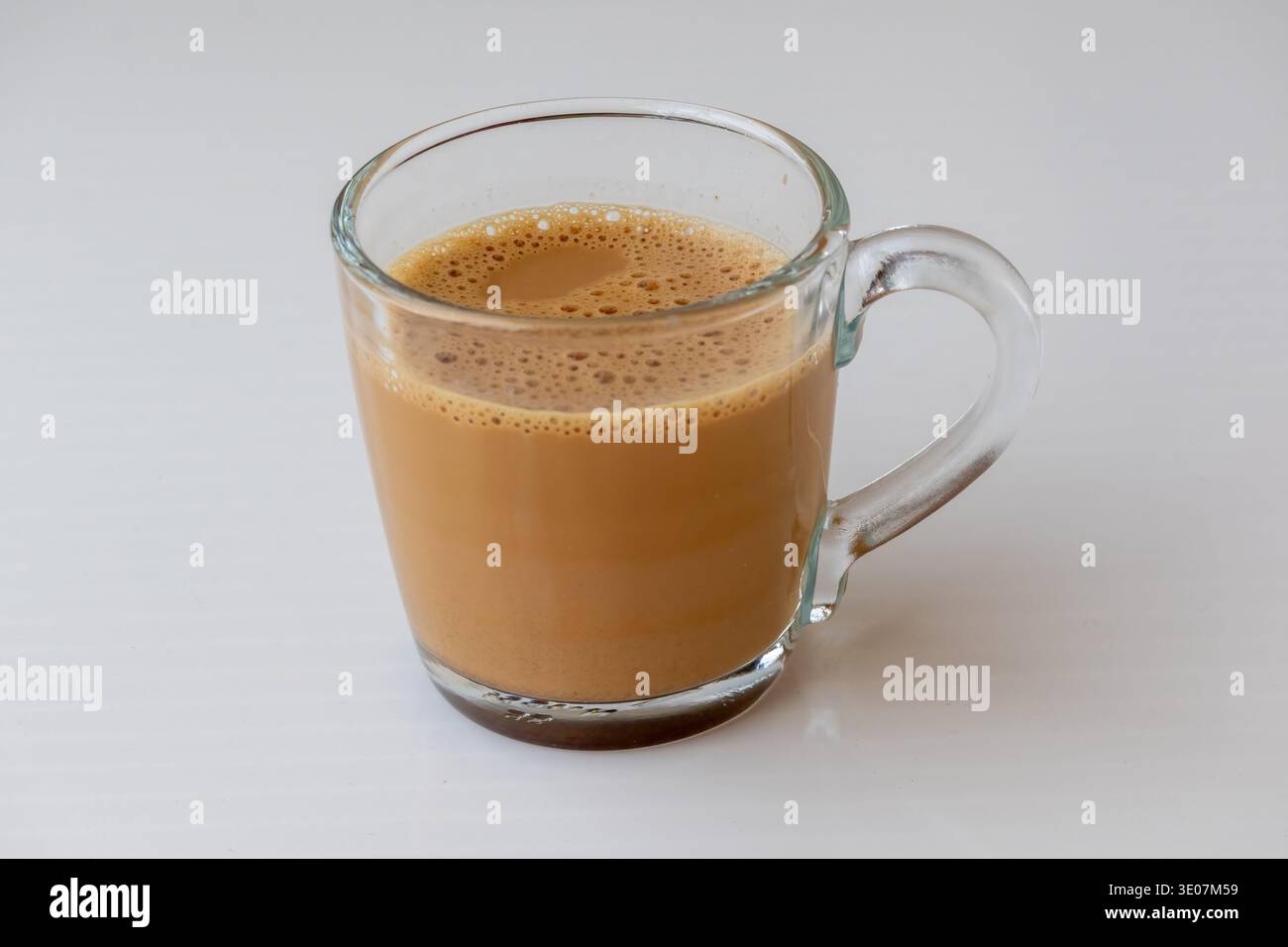 Delizioso masala chai indiano aromatico servito in una tazza trasparente con schiuma ricca su una superficie bianca. Ideale per il marketing di uno stile di vita sano Foto Stock
